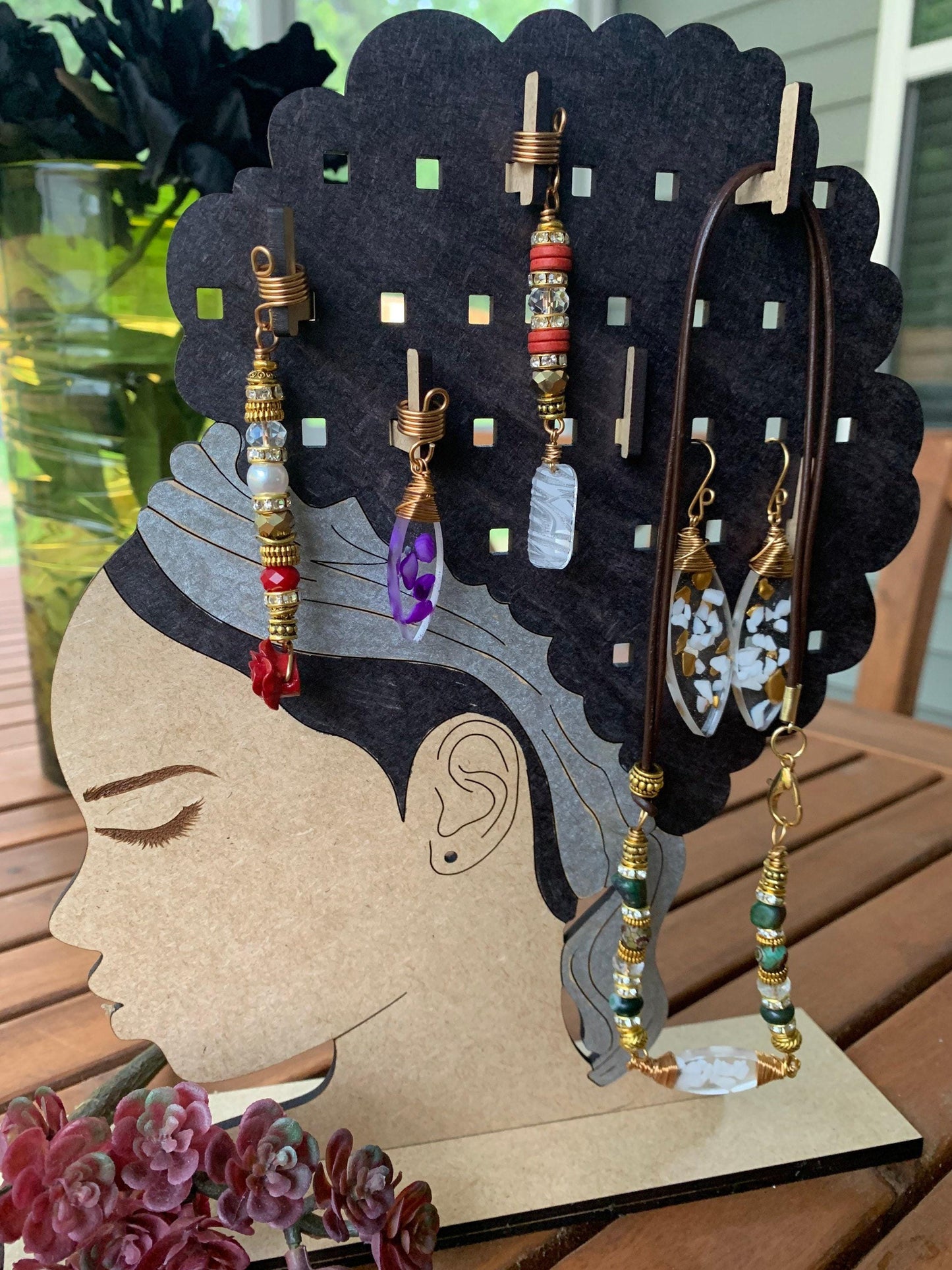 A wooden jewelry display featuring a stylized female head silhouette with various earrings and necklaces hanging from it.