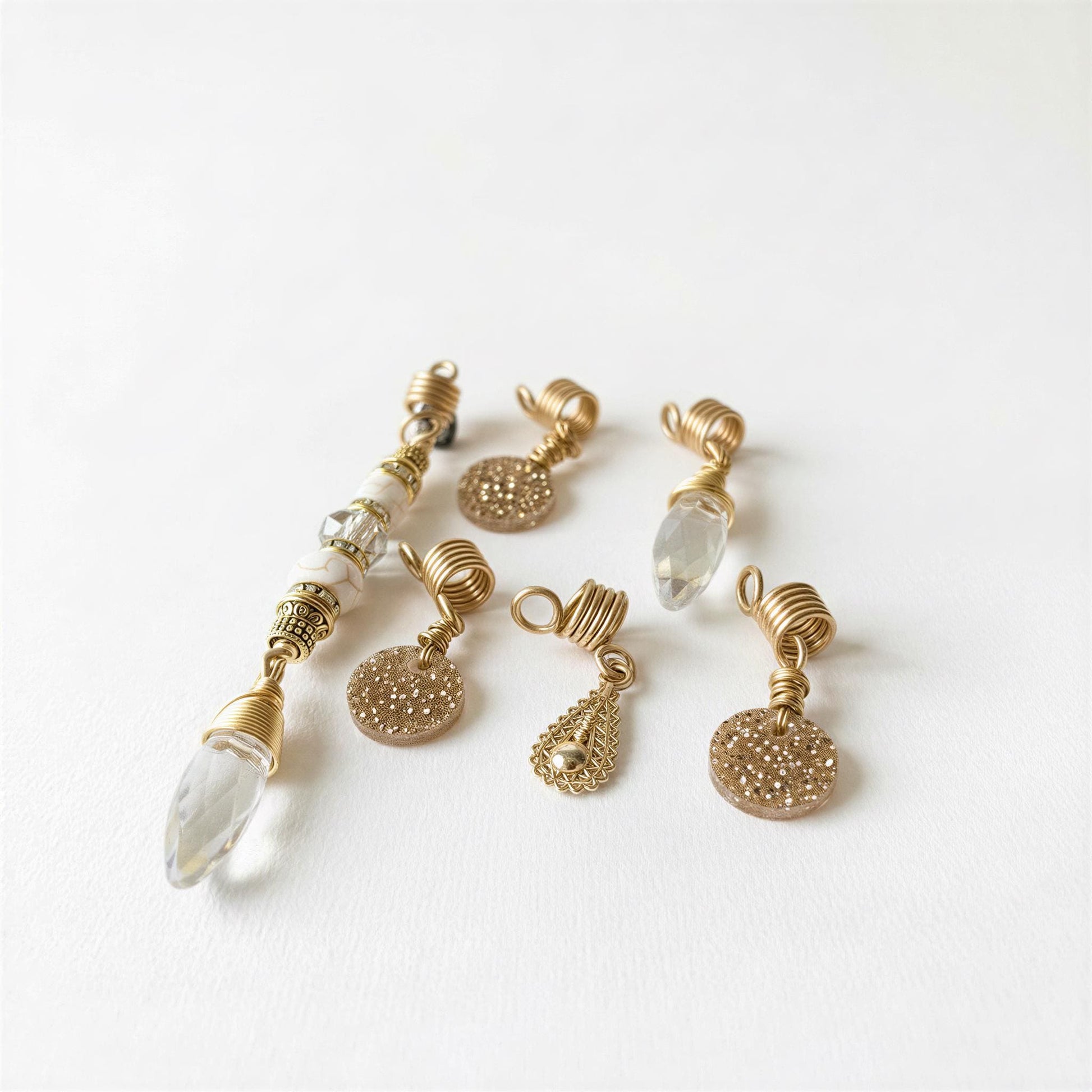 a collection of six gold-colored earrings with various shapes and designs, including clear and round pendants, arranged on a white background.