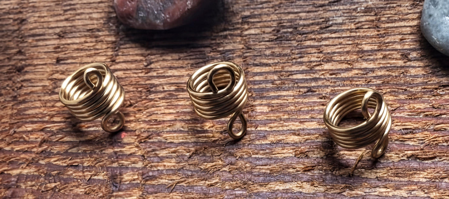 Three gold spiral earrings are arranged on a wooden surface.