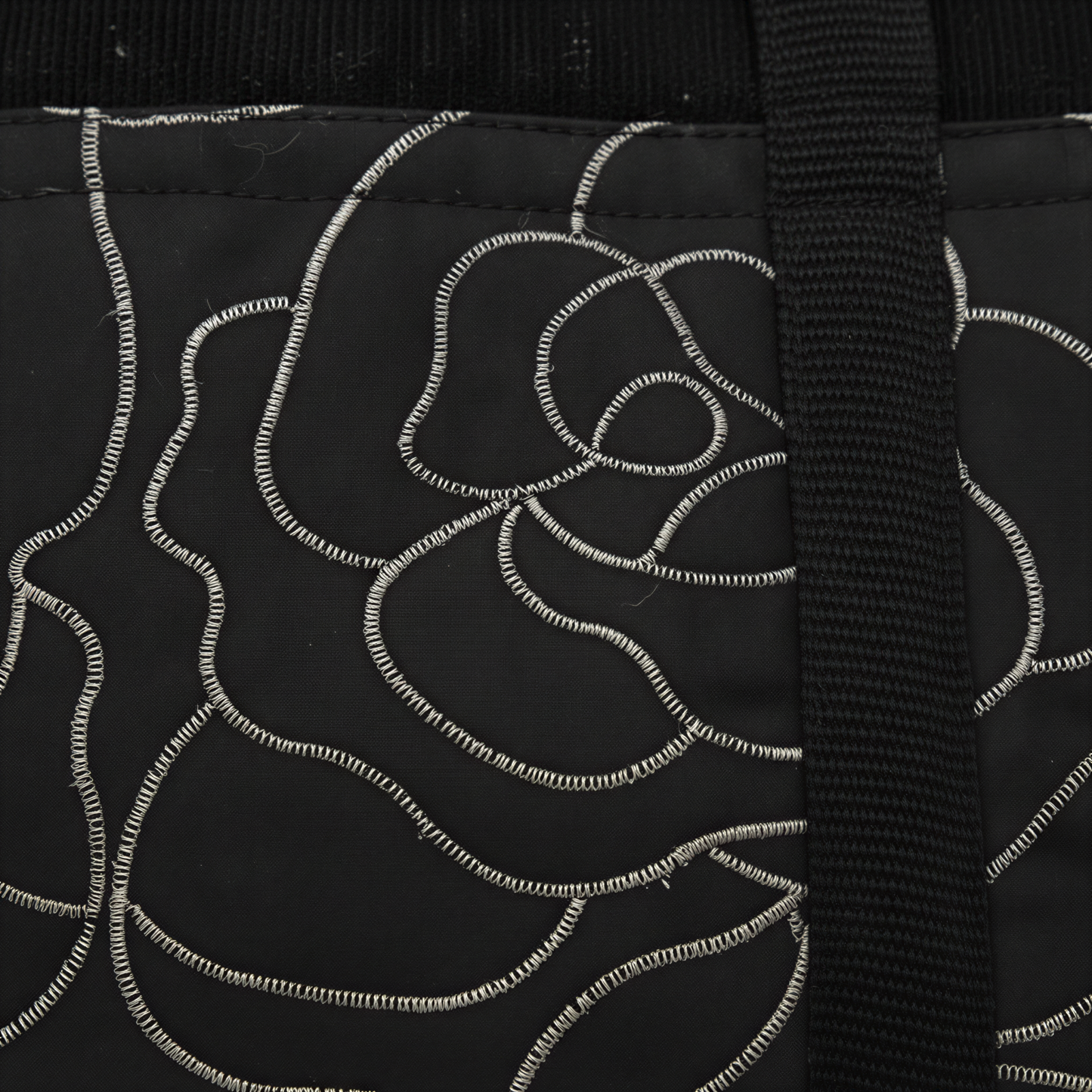 a close-up view of a black fabric with a white floral pattern. The fabric appears to be a piece of clothing or textile, with a black strap or cord visible on the right side.