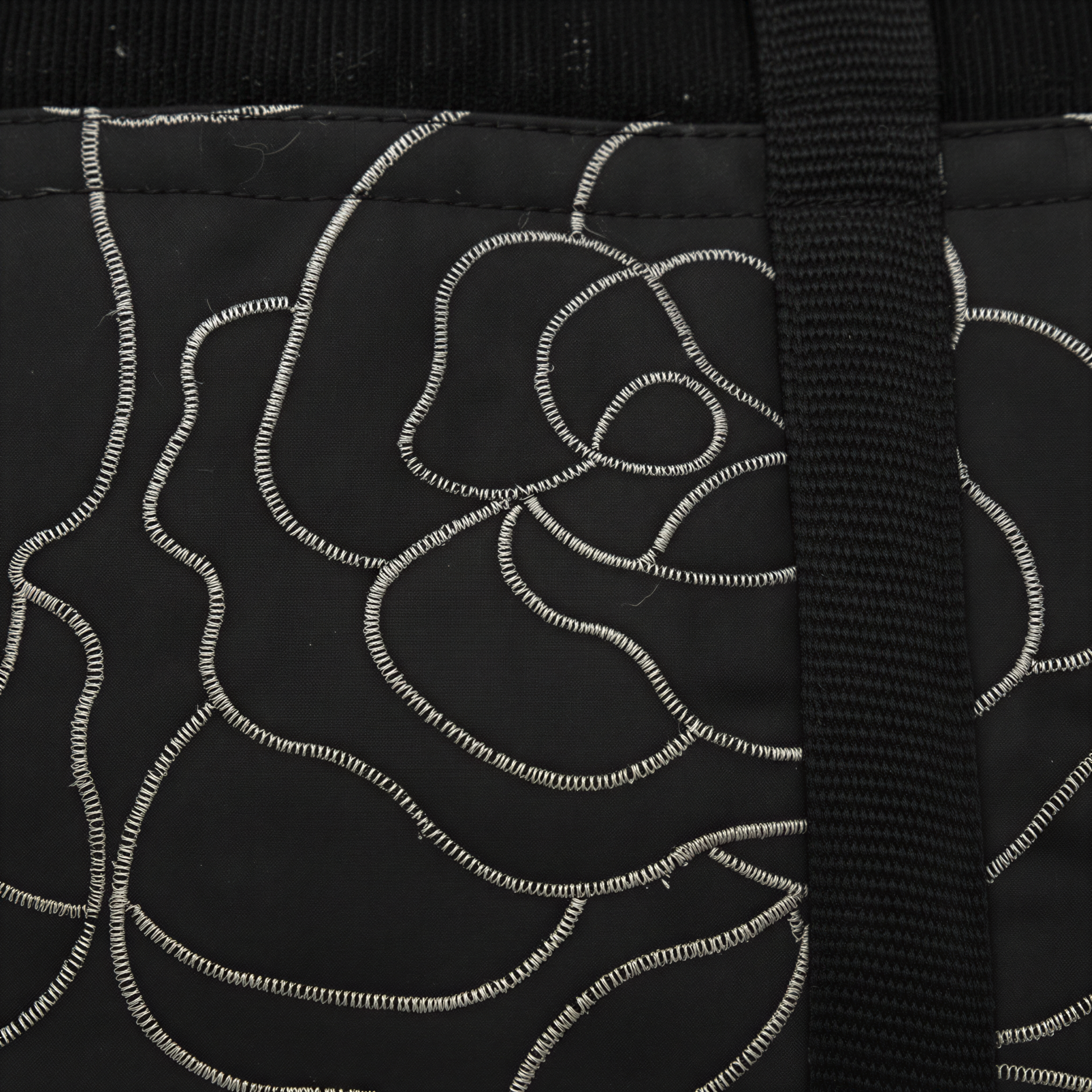 a close-up view of a black fabric with a white floral pattern. The fabric appears to be a piece of clothing or textile, with a black strap or cord visible on the right side.