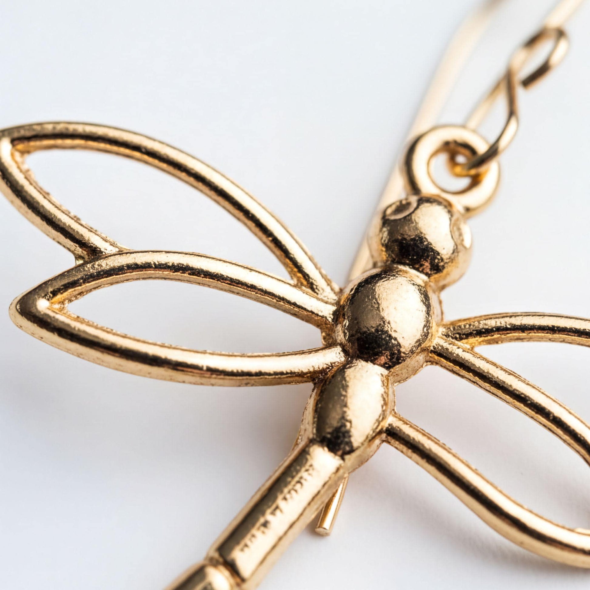 A close-up image of a gold-colored metal dragonfly pendant or earring.