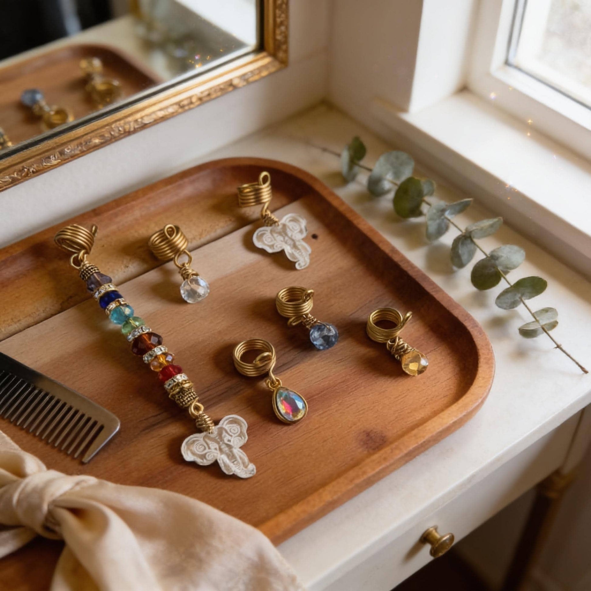A wooden tray displaying various jewelry items, including earrings, rings, and a pendant, placed on a white dresser near a window.