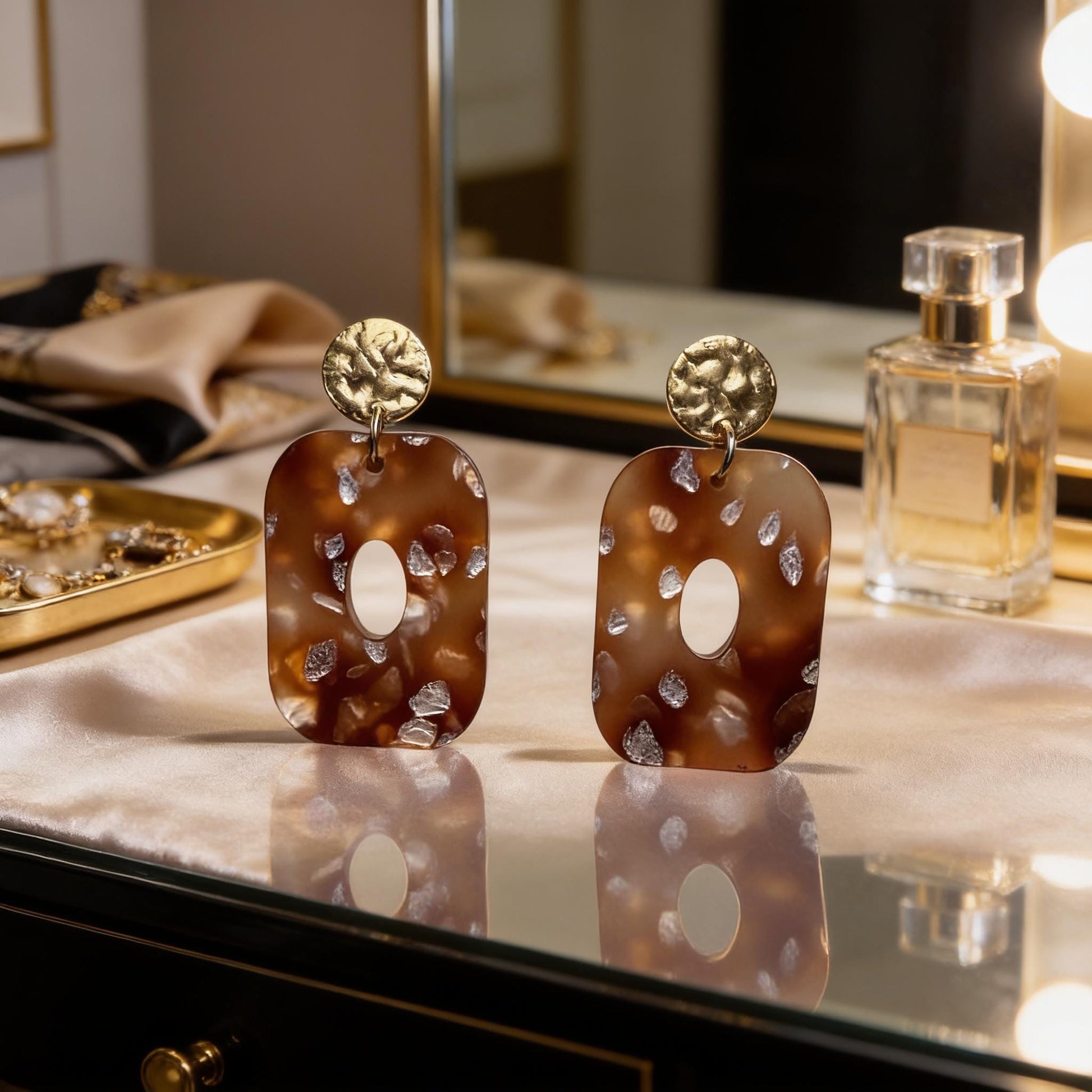a pair of brown earrings with a polka dot pattern, placed on a reflective surface. In the background, there is a mirror and a bottle of perfume, suggesting a setting where the earrings are being displayed.
