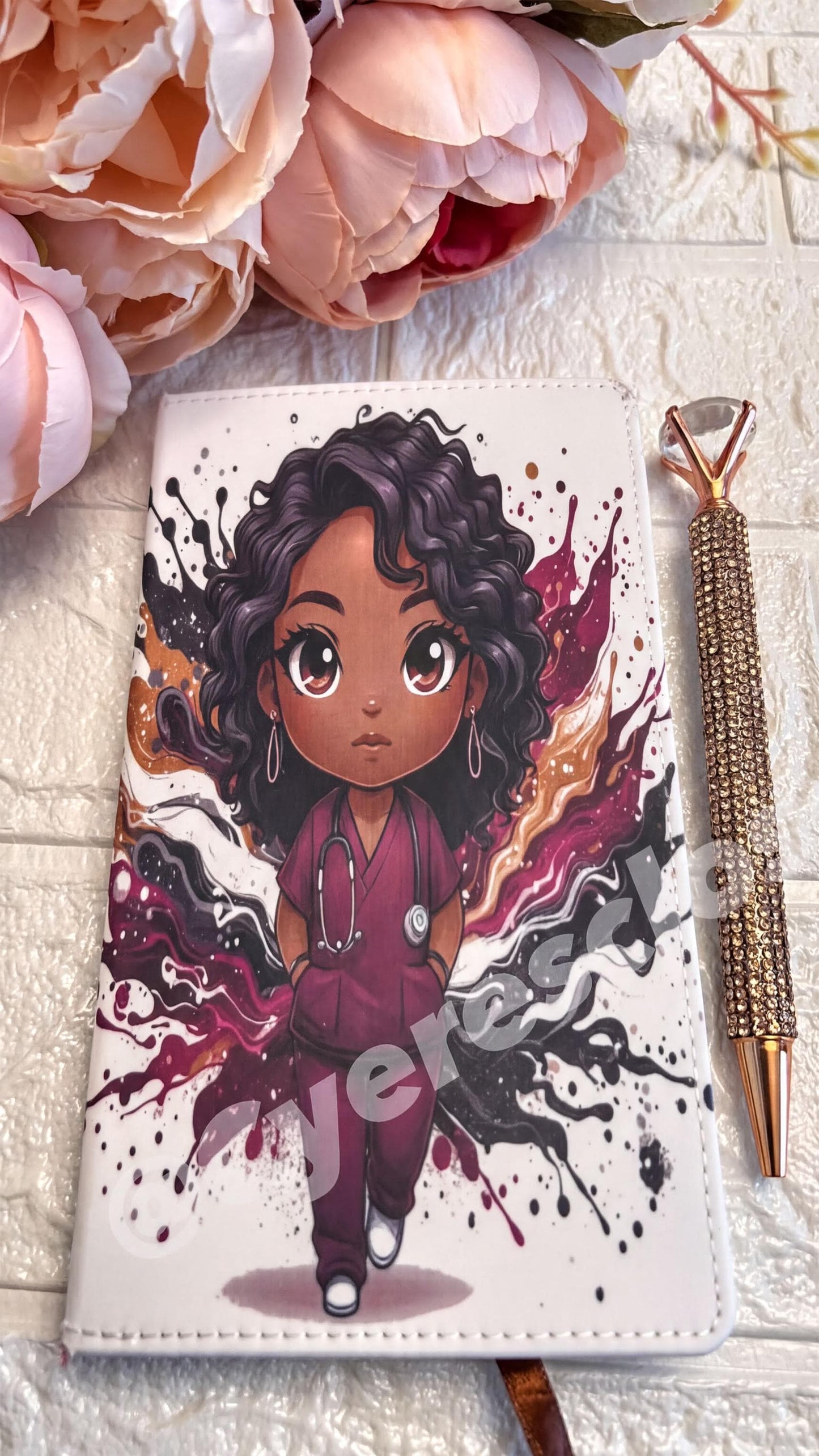 a white notebook with a colorful illustration of a young girl wearing a stethoscope, surrounded by splashes of color. The notebook is placed on a white surface, and there is a pen next to it.