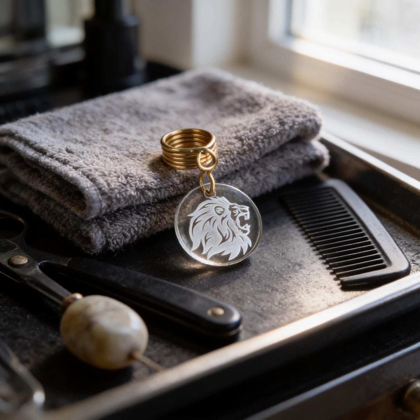 a clear keychain with a lion's head design, placed on a tray alongside a pair of scissors and a comb.