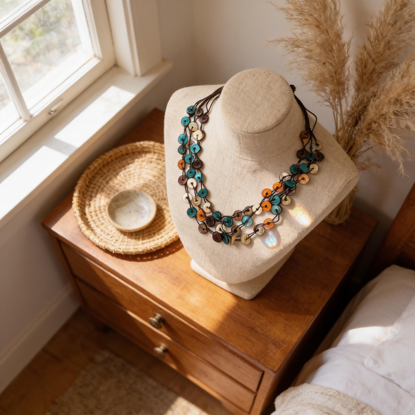 A beige mannequin head wearing a colorful necklace with various beads and stones, placed on a wooden dresser next to a woven basket and a small bowl.
