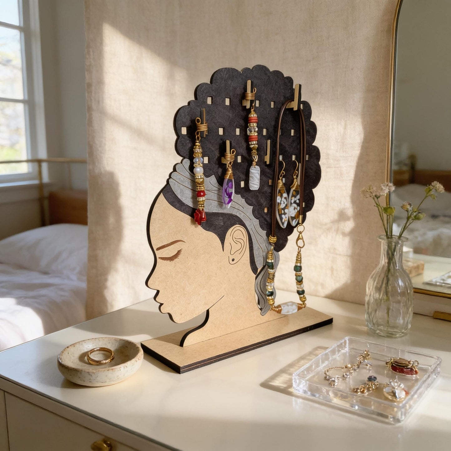 A wooden jewelry stand with a woman's head silhouette and various earrings and necklaces displayed on it, placed on a white dresser in a bedroom setting.