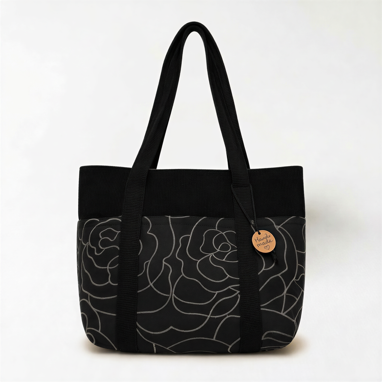 A black tote bag with a floral pattern on the front and handles.