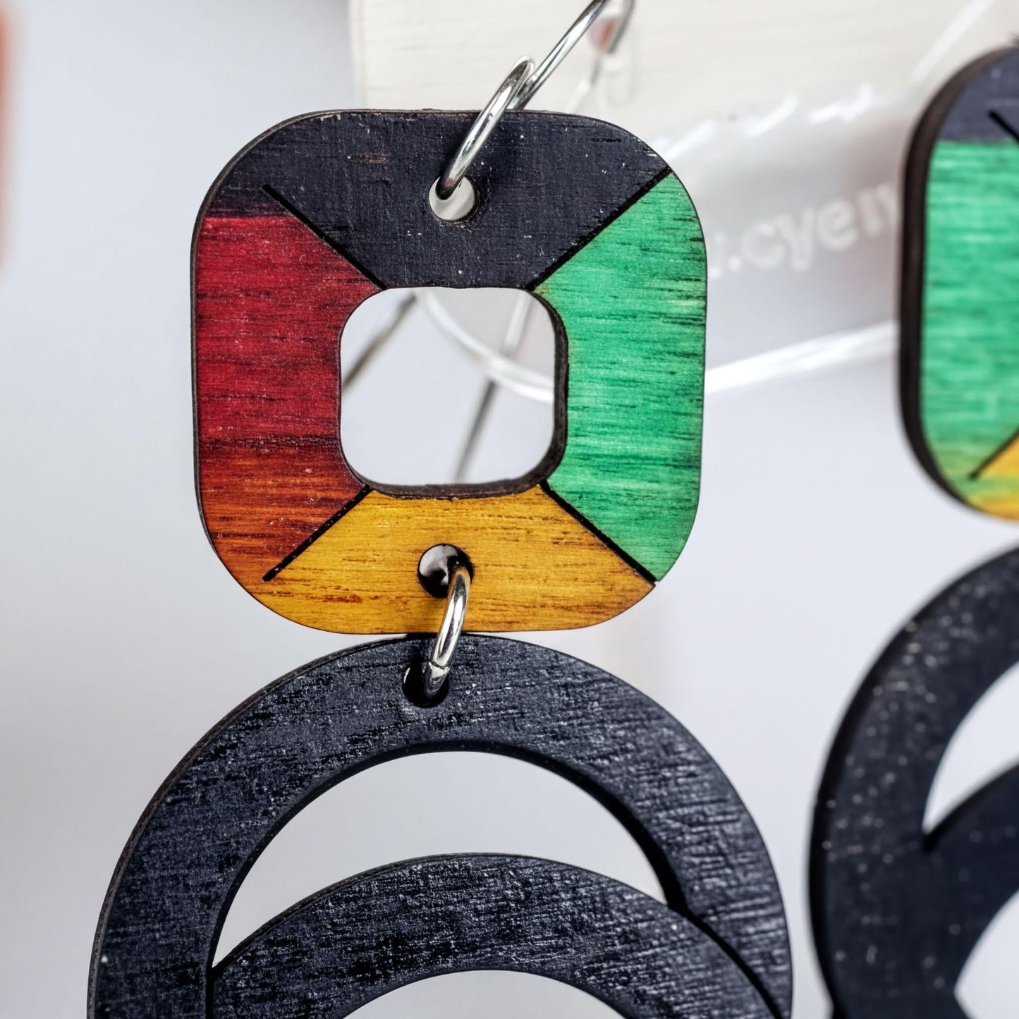 A pair of colorful earrings with a geometric design, featuring a combination of red, yellow, green, and black colors.