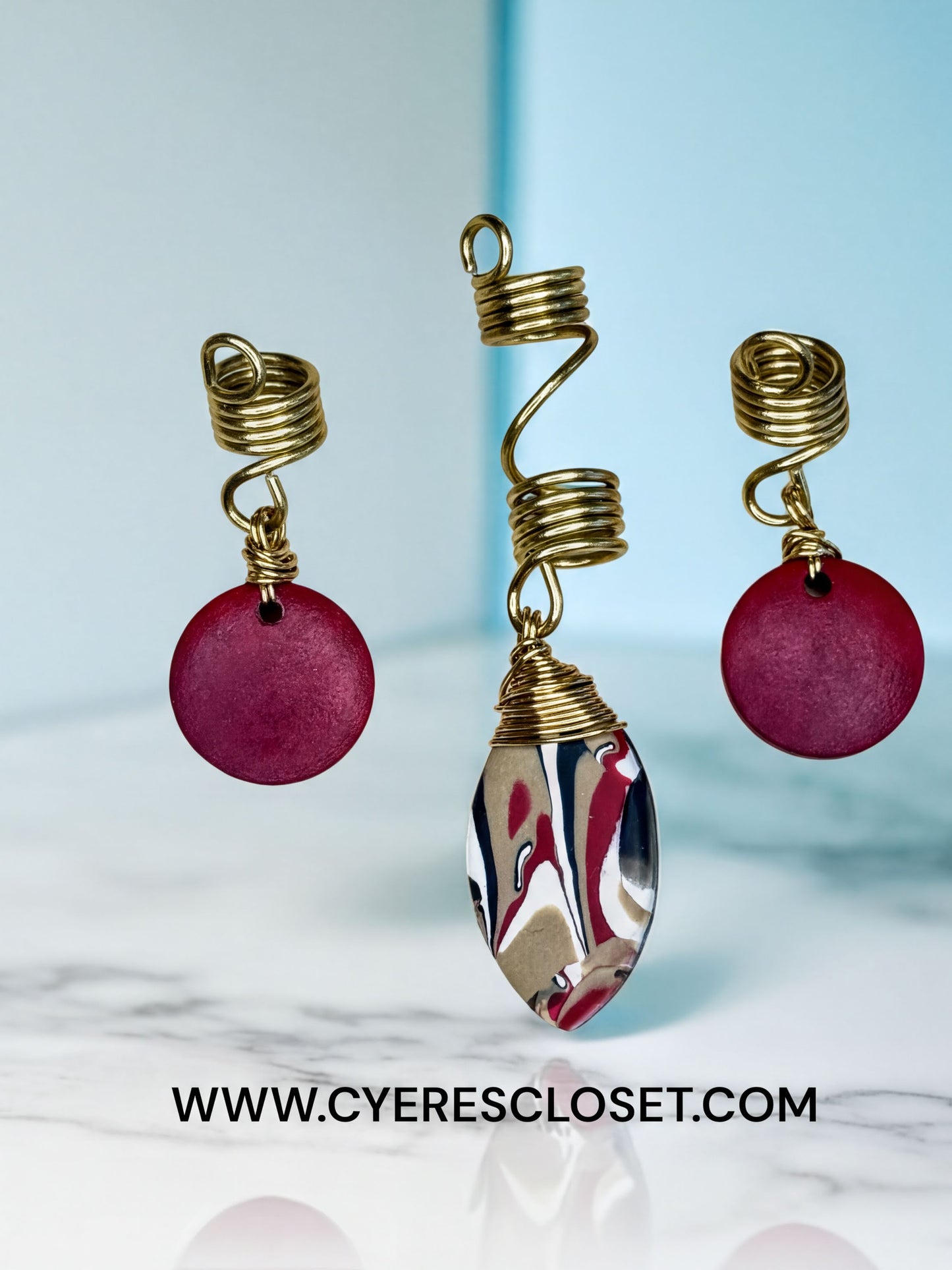 a pair of earrings and a hair clip with a unique, abstract design. The earrings are made of a shiny, metallic material and have a red circular shape, while the hair clip has a spiral design and is made of a shiny, metallic material. The image is set against a light blue background, and there is a watermark at the bottom that reads "www.CYERRESCLOSET.com".