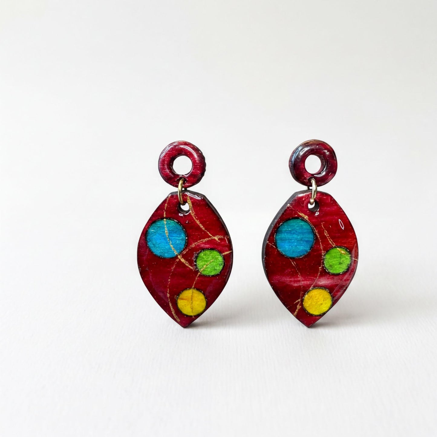 A pair of red earrings with colorful polka dots and a metallic ring hanging from the top.