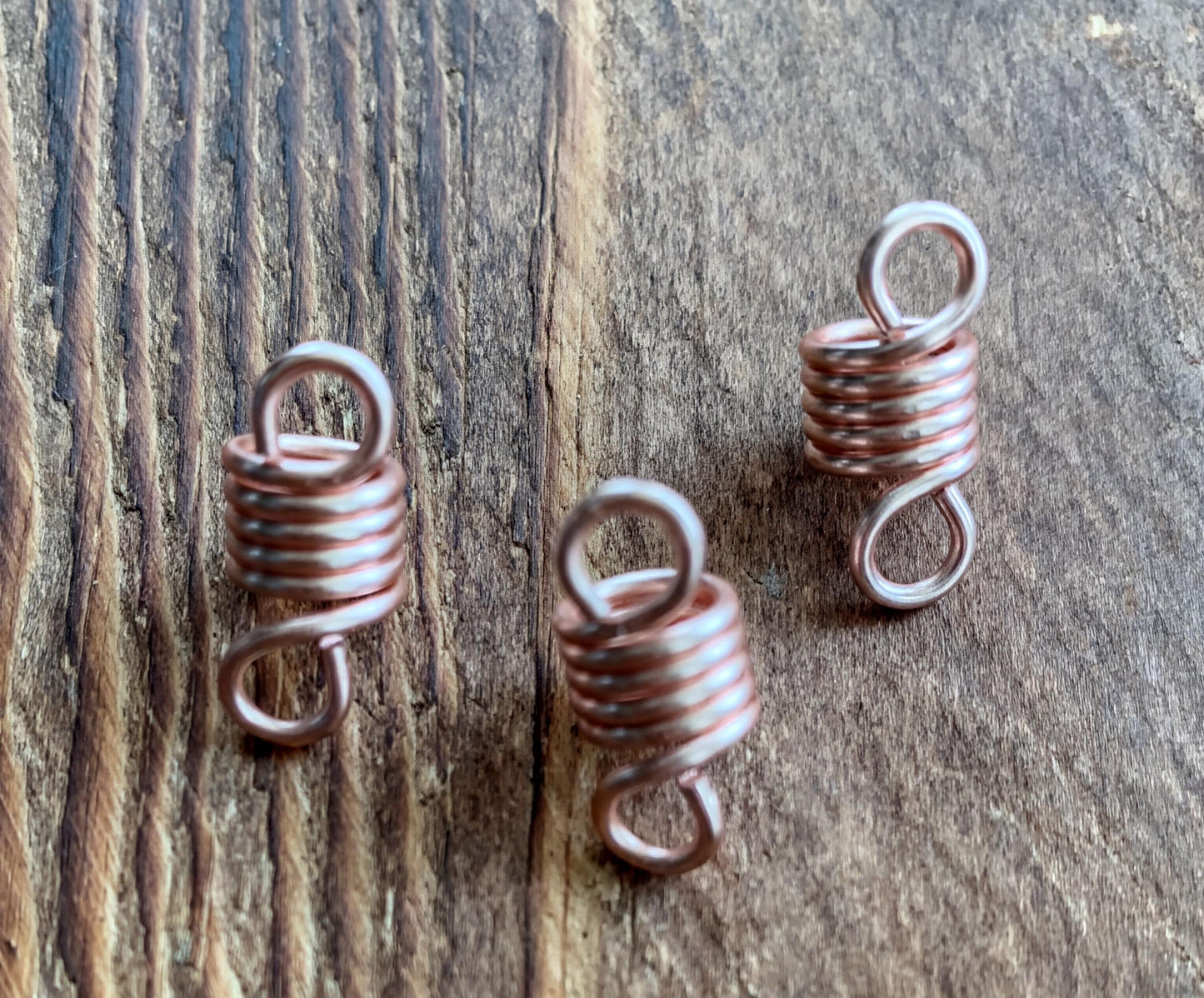 three copper-colored spiral coiled springs resting on a wooden surface.