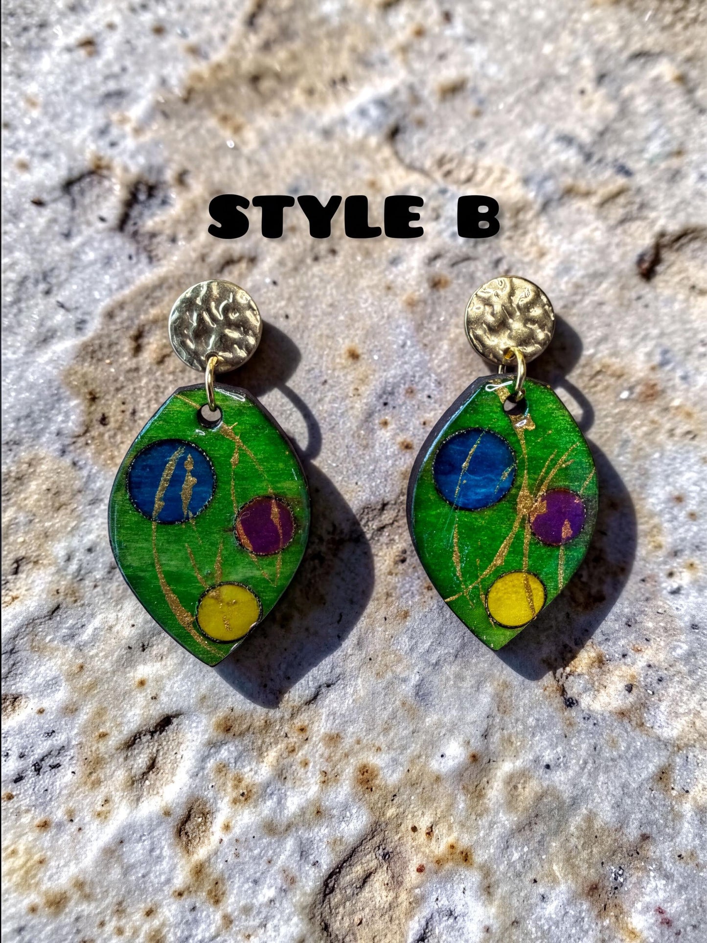 A pair of earrings with green leaves and colorful circles on a textured surface.