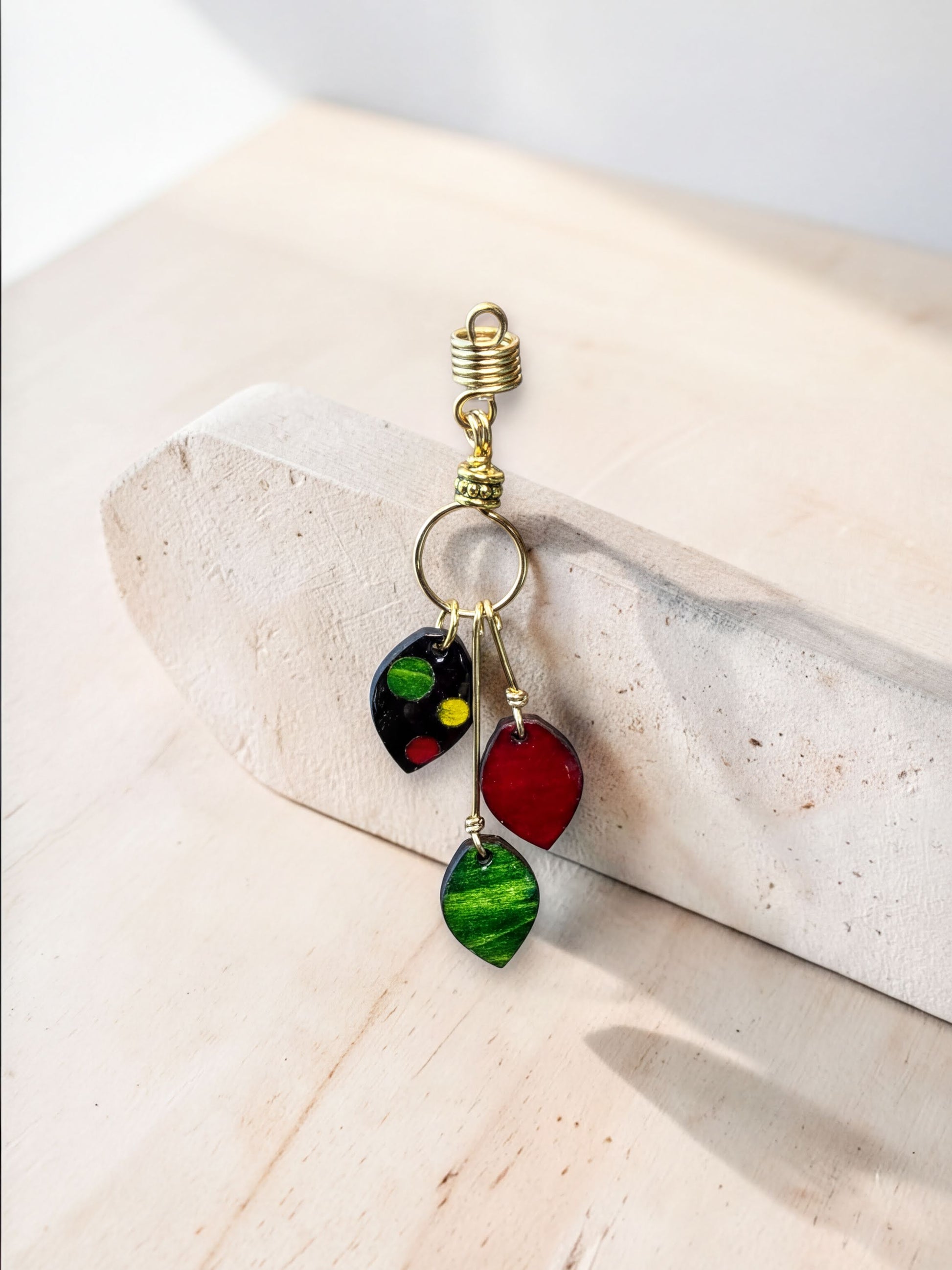A decorative earring with colorful stones, including red, green, and black, hanging from a gold hook on a white surface.