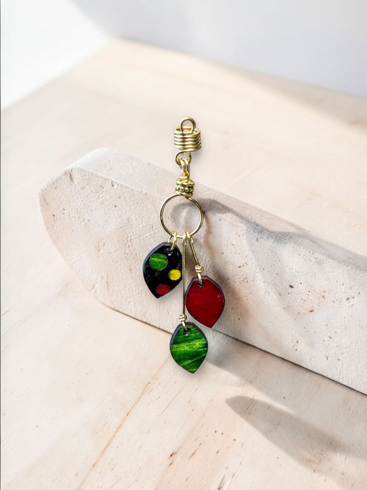 A decorative earring with colorful stones, including red, green, and black, hanging from a gold hook on a white surface.
