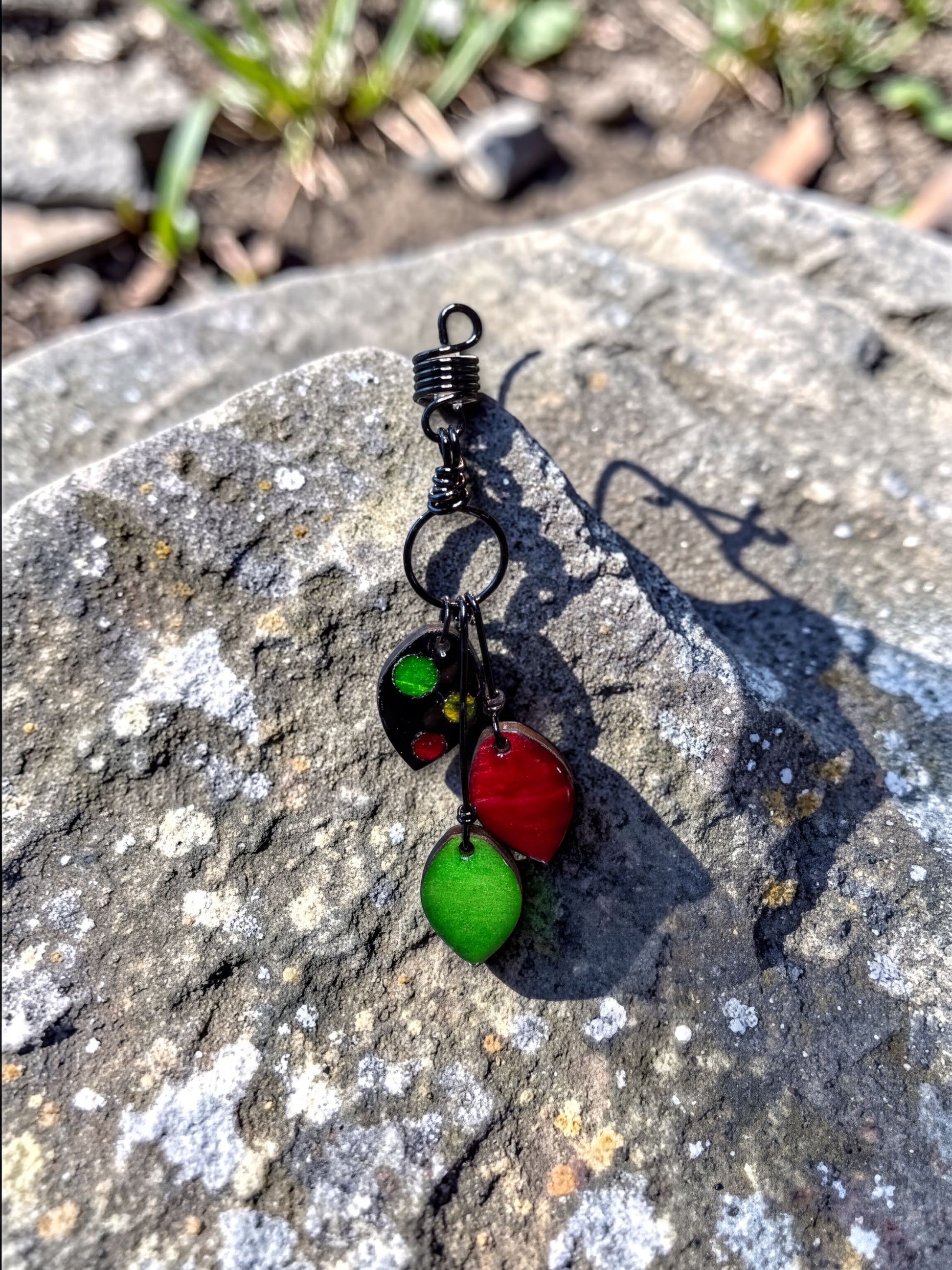 A black wire earring with three colorful beads hanging from it, resting on a rock.