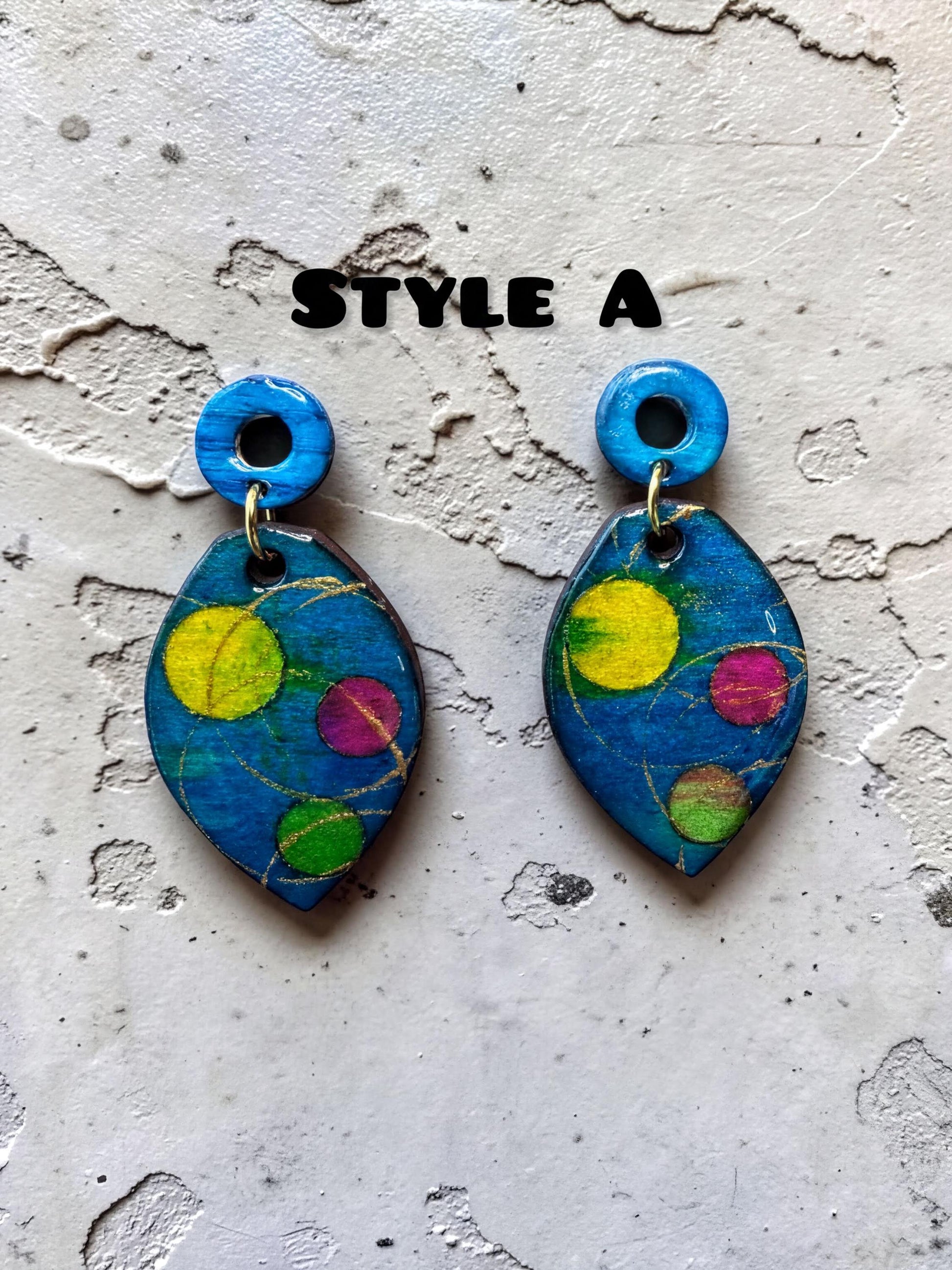 a pair of colorful earrings with blue and yellow designs, placed on a textured surface.
