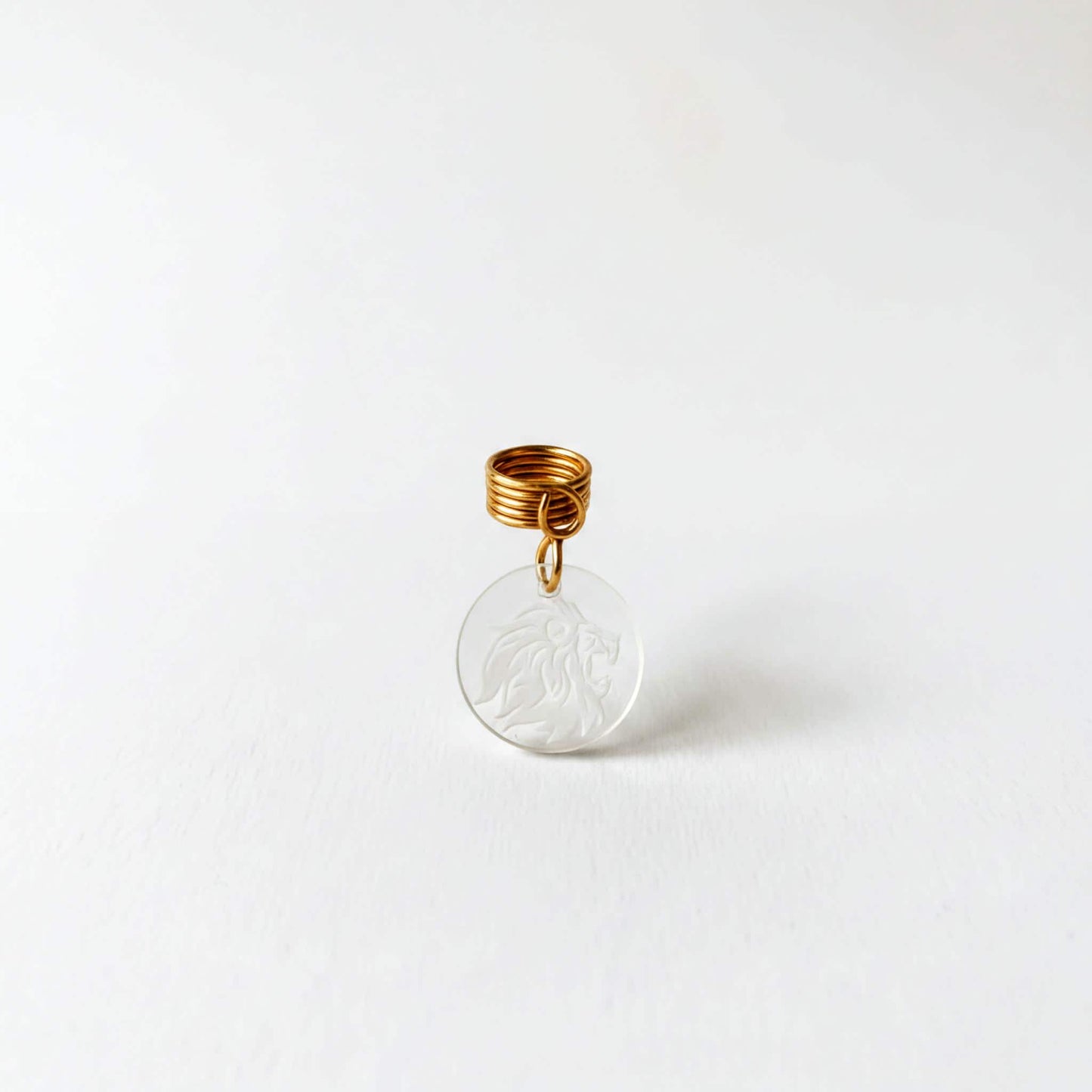 A clear pendant with a gold spiral attached to it, featuring an engraved lion design.