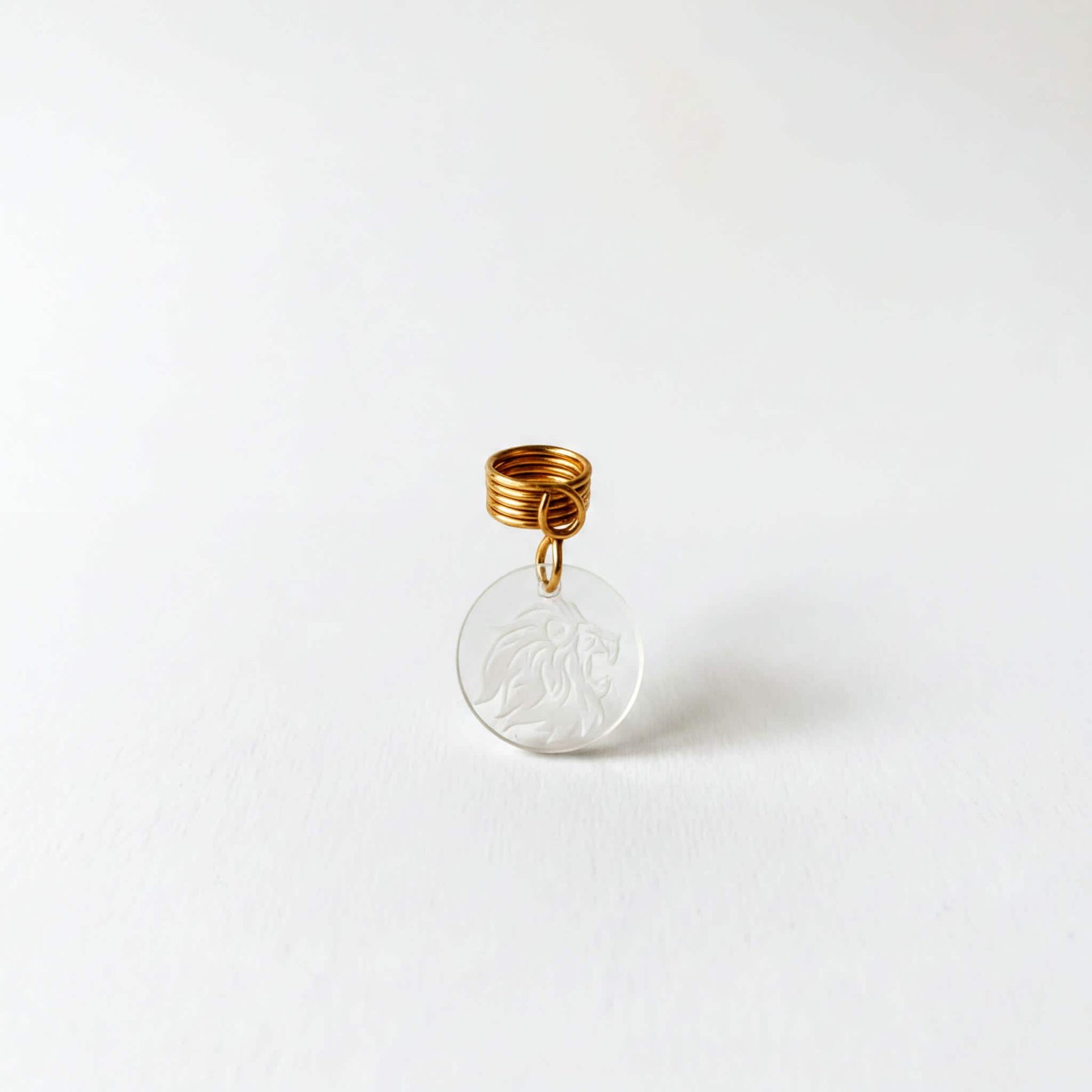 A clear pendant with a gold spiral attached to it, featuring an engraved lion design.