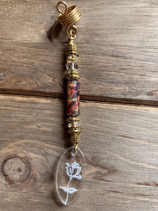 A decorative hair accessory with a clear oval pendant featuring a white flower design, hanging from a gold-colored metal loop.