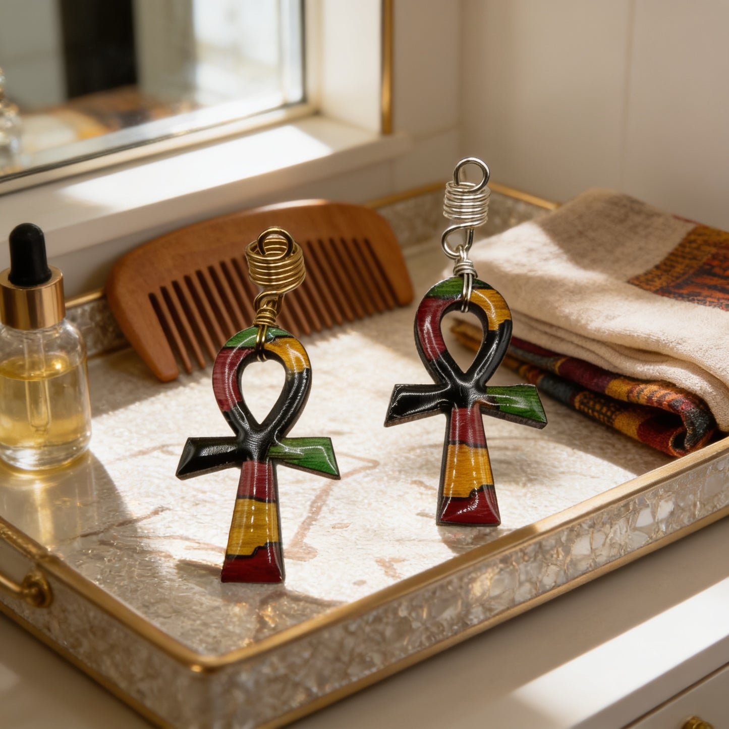 two colorful, abstract-shaped pendants or charms, possibly resembling ancient Egyptian symbols, placed on a tray alongside a wooden comb and a bottle.