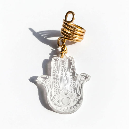 A clear glass hand charm with a gold spiral attached to it, resting on a white background.