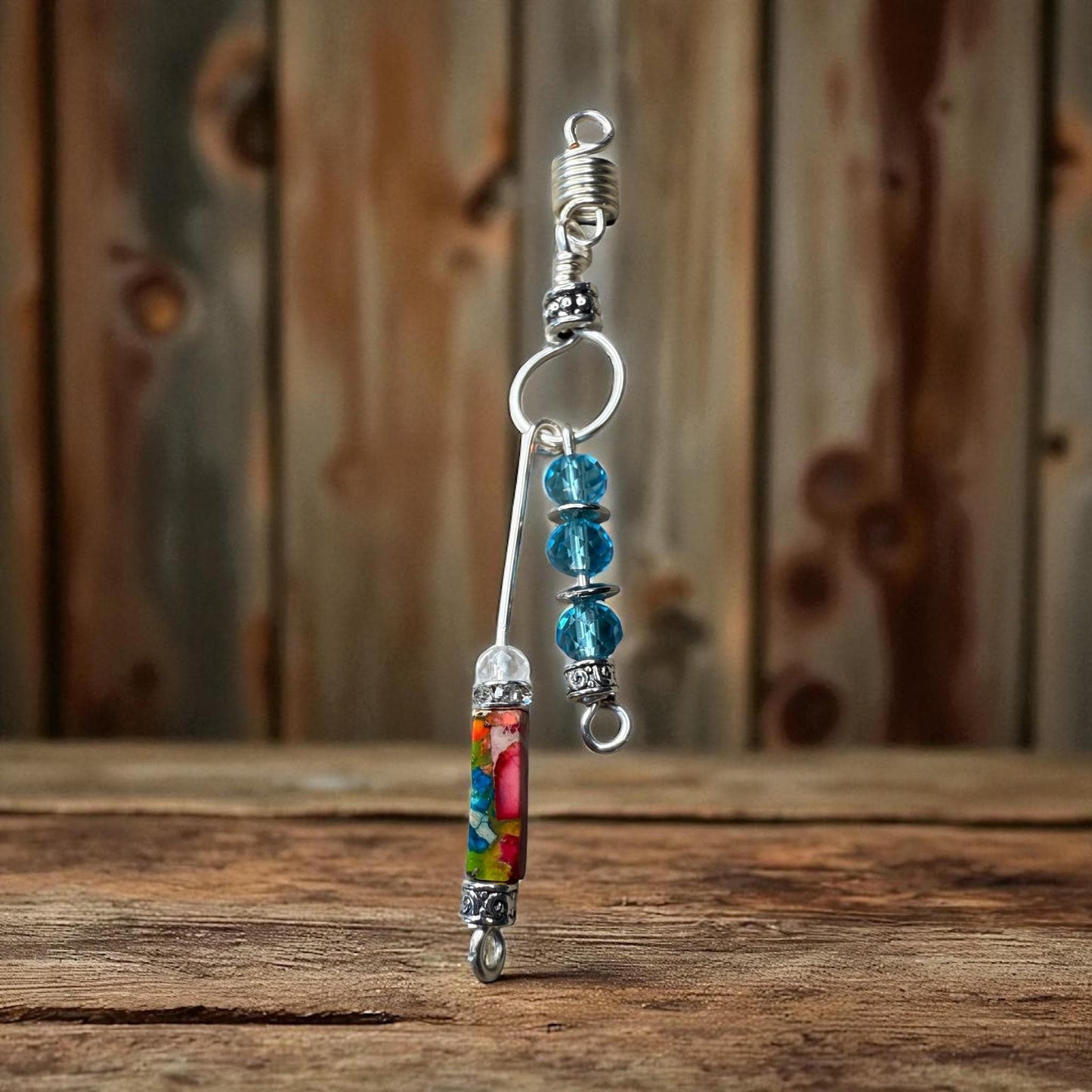 A colorful beaded charm with a metal hook attached to it, displayed on a wooden surface against a wooden background.