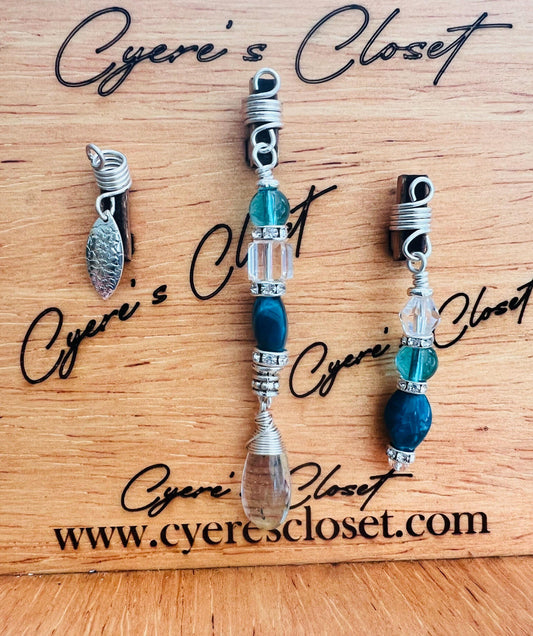 a collection of jewelry pieces, including necklaces and earrings, arranged on a wooden surface. The jewelry appears to be made of silver and clear materials, with various beads and charms attached to the pieces. The image does not contain any text, and the focus is on the jewelry and its arrangement.