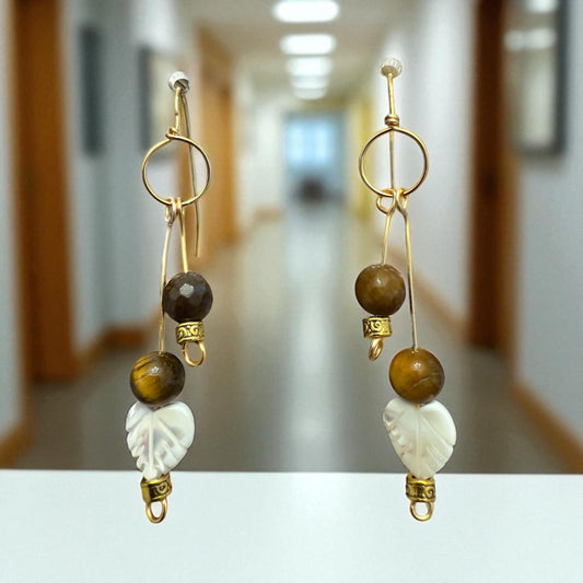A pair of gold earrings with various beads and leaf-shaped charms hanging from the ear hooks.