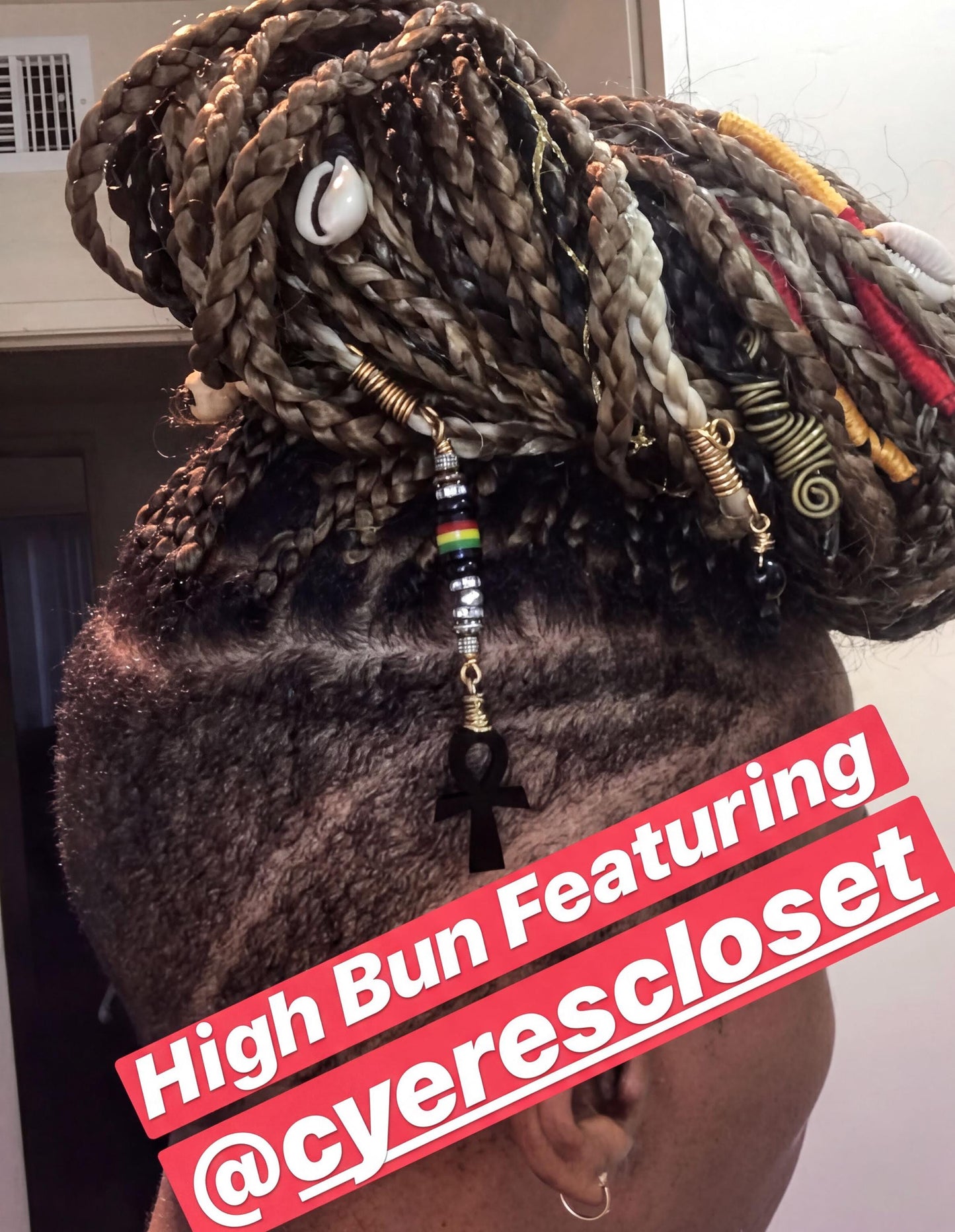 a person with braided hairstyle and various accessories, including beads and a pendant, which are part of a hair styling.