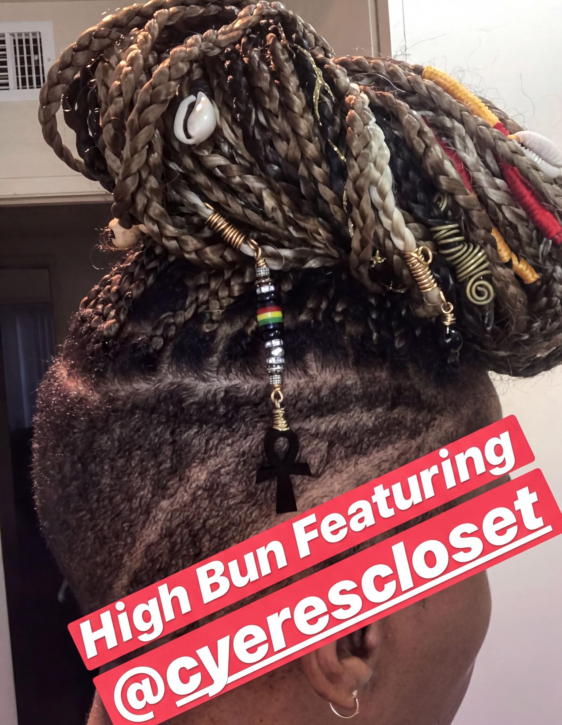 a person with braided hairstyle and various accessories, including beads and a pendant, which are part of a hair styling.