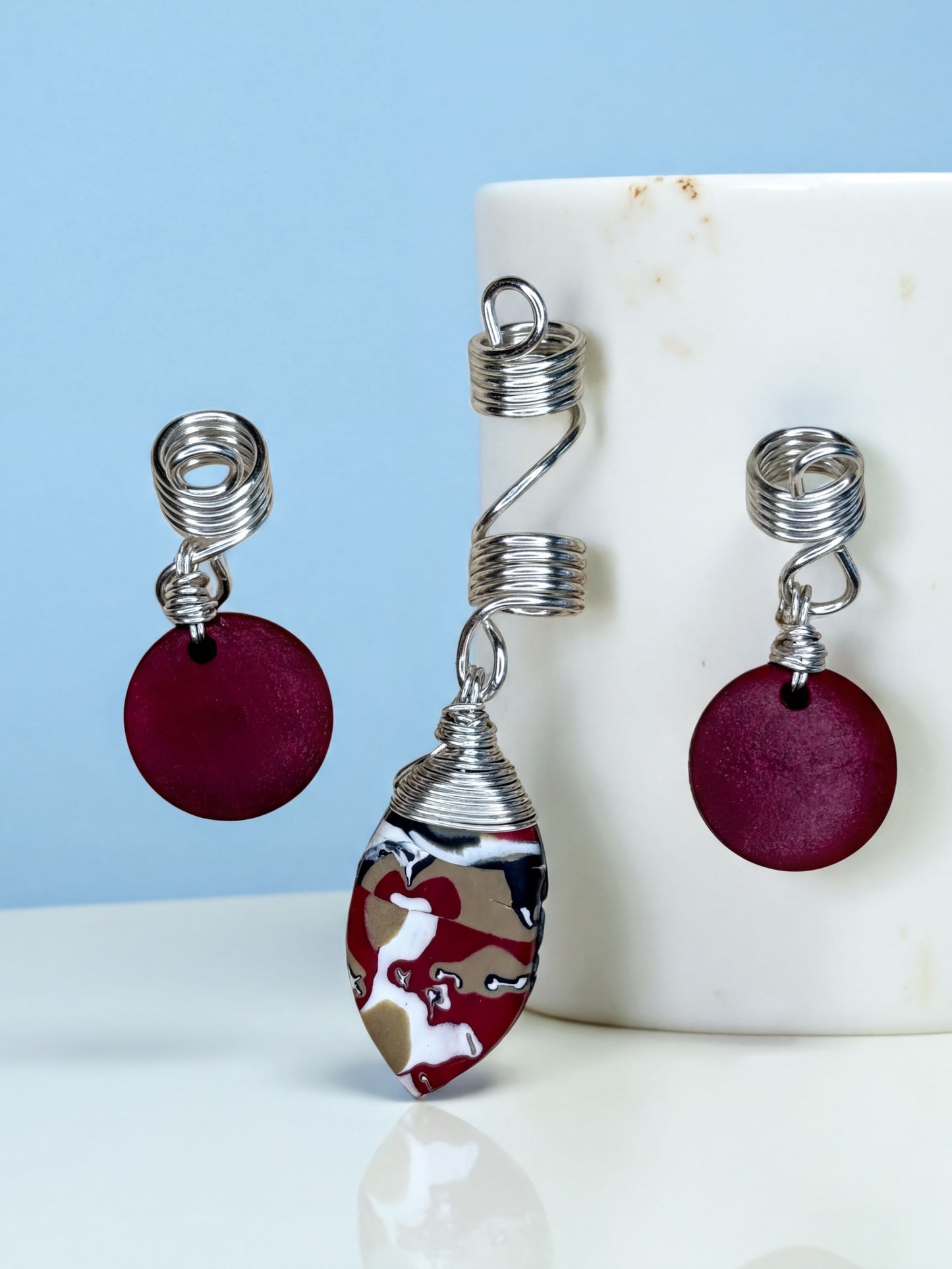 a pair of earrings and an ear cuff with a maroon color and a metallic twist design.