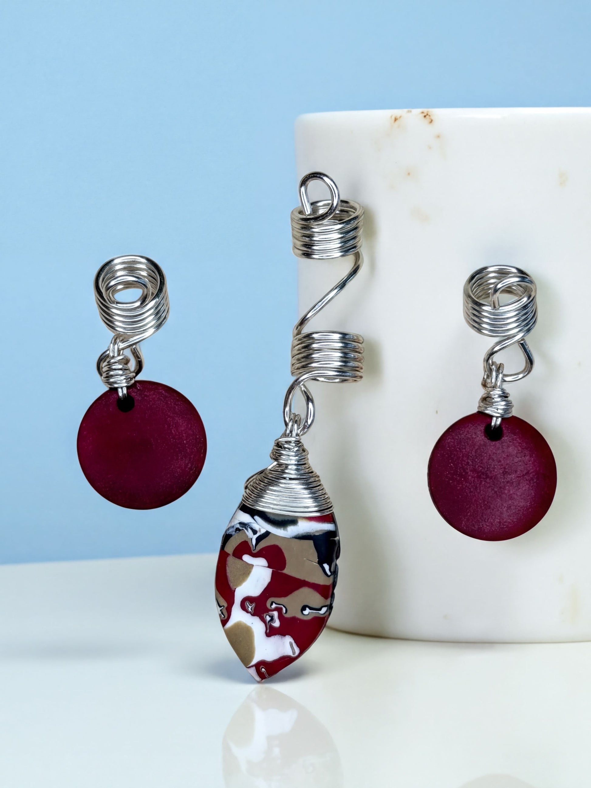 a pair of earrings and an ear cuff with a maroon color and a metallic twist design.