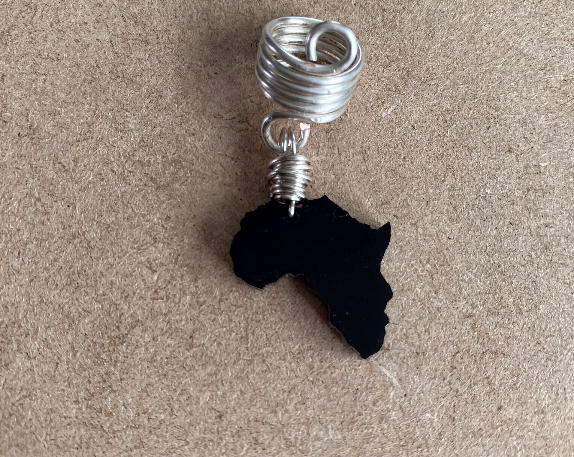 A silver spiral earring with a black African continent pendant is shown against a textured beige background.