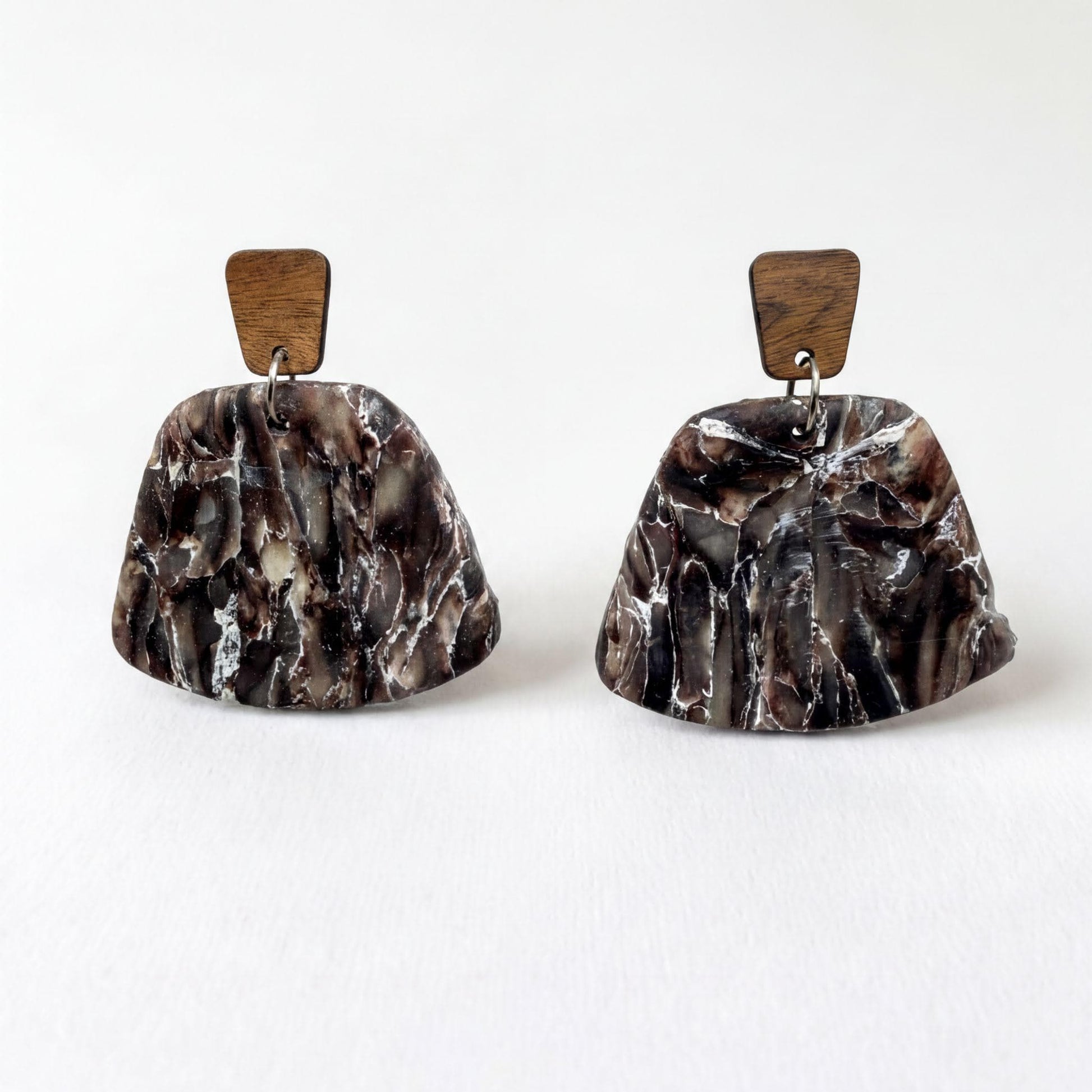 A pair of earrings with a marble-like texture and wooden accents, displayed against a white background.