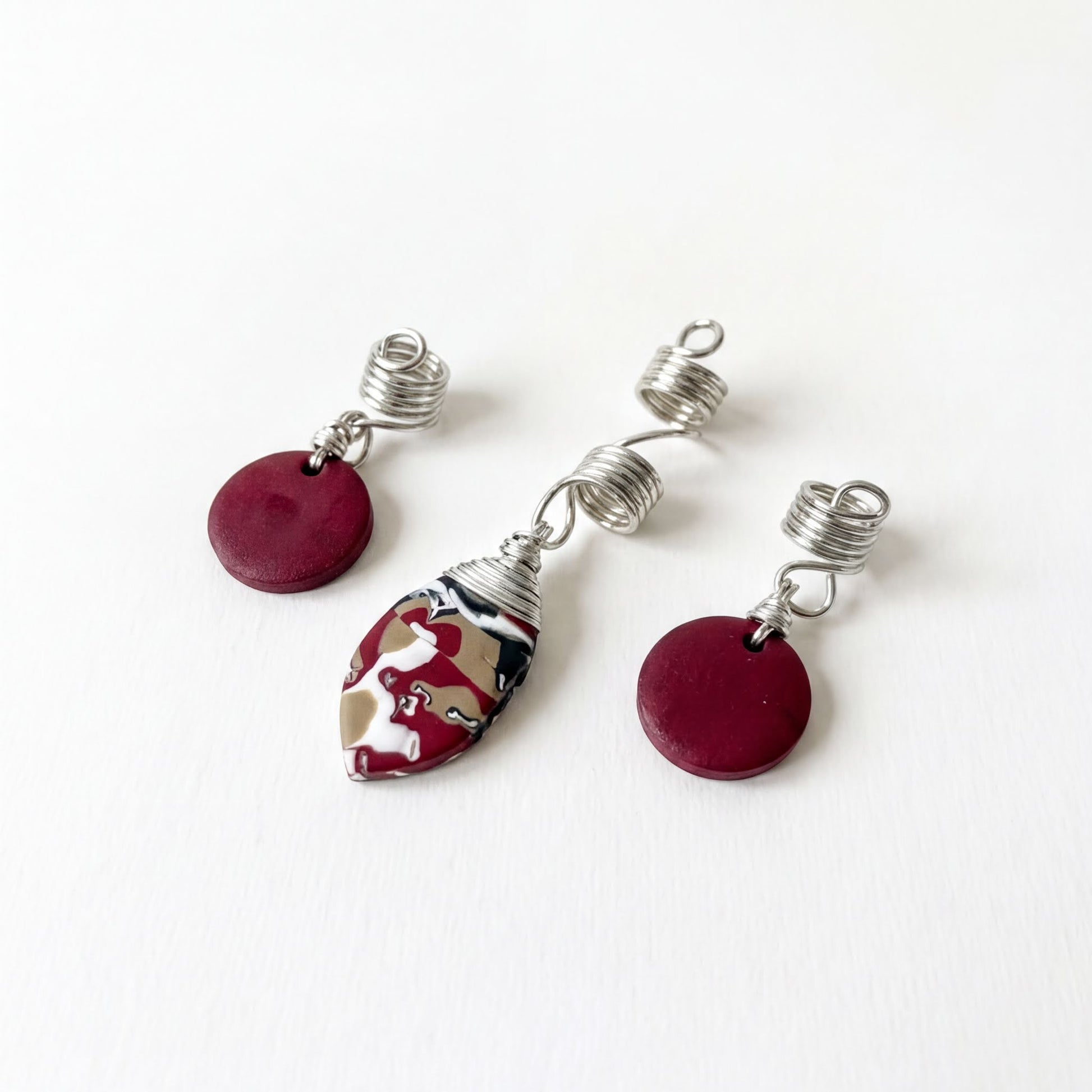 a pair of earrings and a hair clip with a maroon color, placed on a white surface.