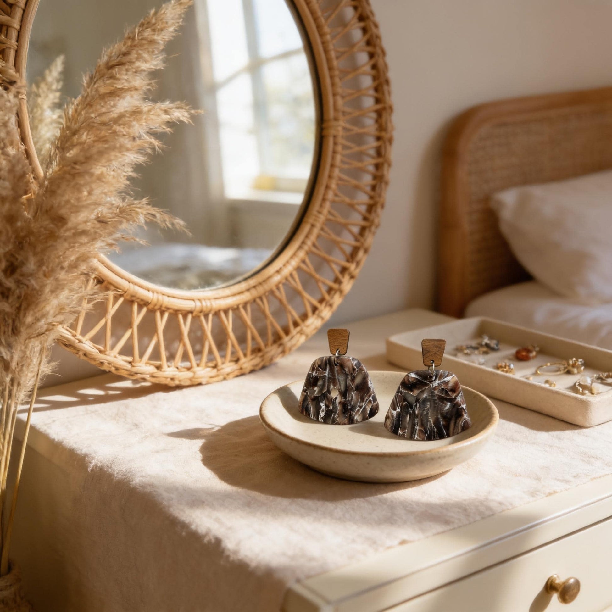 a bedroom setting with a round mirror, a wooden headboard, and a bed. On the bedside table, there is a small plate with two decorative earrings, and a tray holding various jewelry pieces.