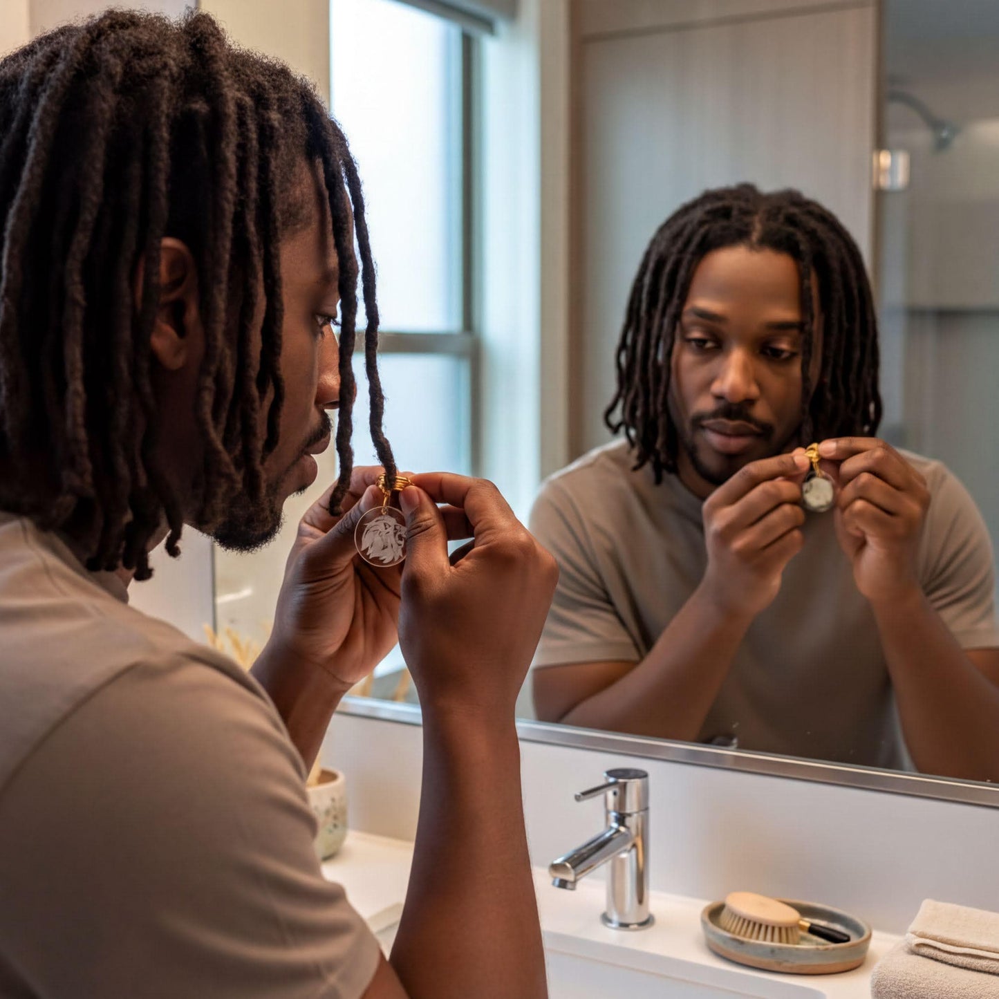 A man with dreadlocks is standing in front of a bathroom mirror, examining his reflection and holding a small object in his hand.