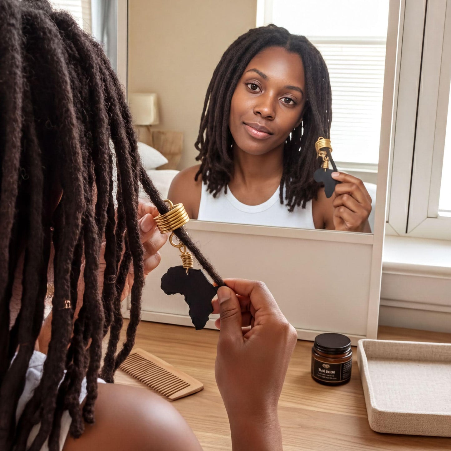 A woman with dreadlocks is holding a hair accessory in front of a mirror, while another woman is visible in the reflection.