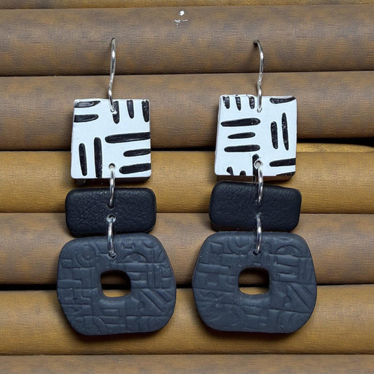 A pair of earrings with a geometric design, featuring black and white shapes and a textured black background.