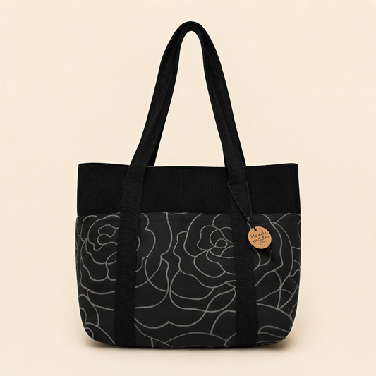 A black and gray floral patterned tote bag with a wooden tag attached.