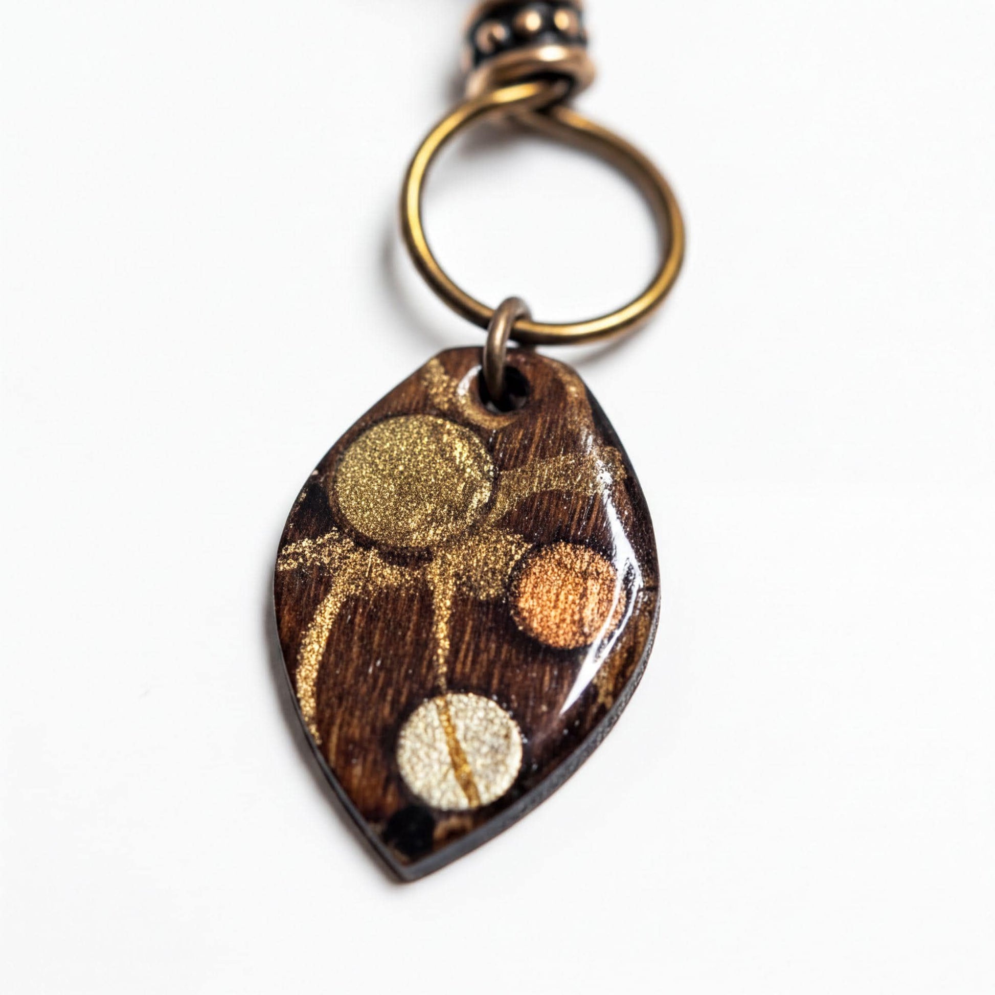 A wooden pendant with a gold and brown design, featuring a circular pattern with three distinct elements.