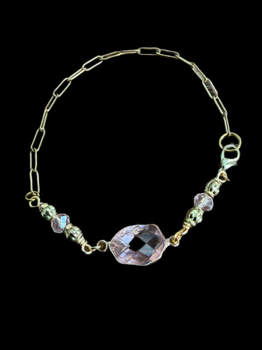 A gold-colored bracelet with a large, clear gemstone in the center, set against a black background.