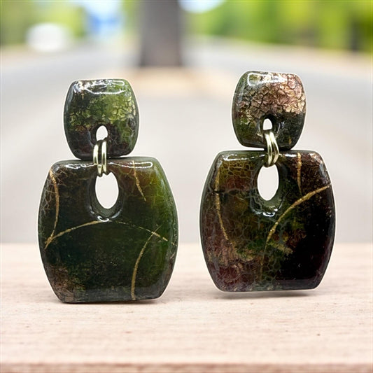 two green, square-shaped earrings with a textured surface, placed on a wooden surface.