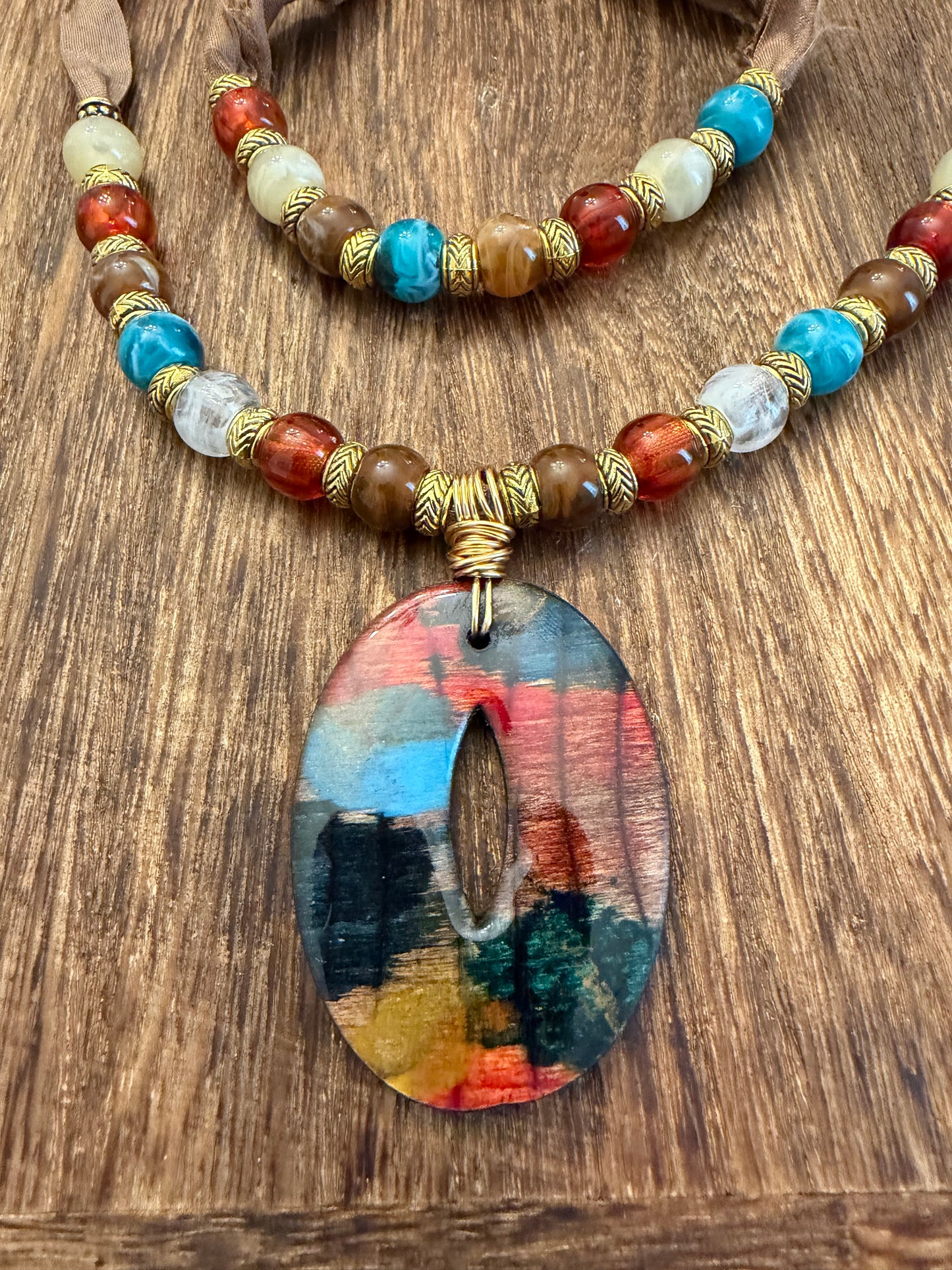 A colorful beaded necklace with a large, circular pendant featuring a vibrant abstract design.