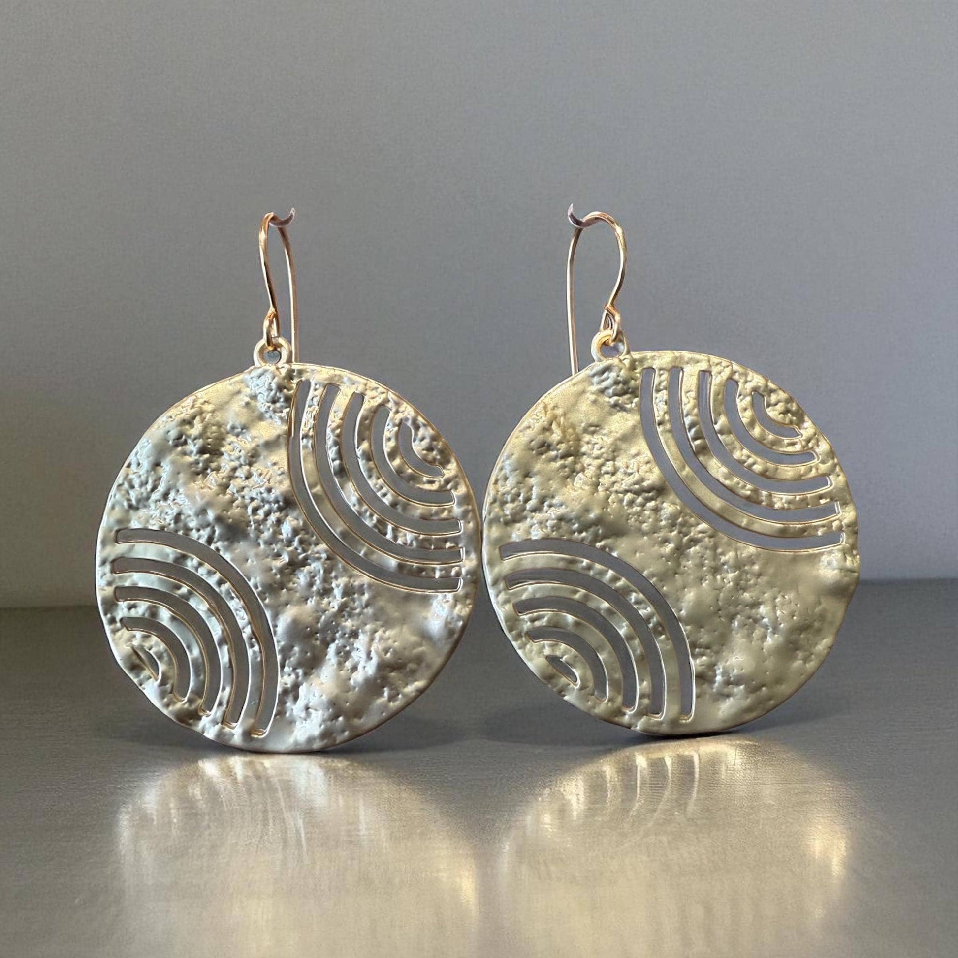 A pair of large, round earrings with a metallic texture and a repeating pattern of waves or circles.