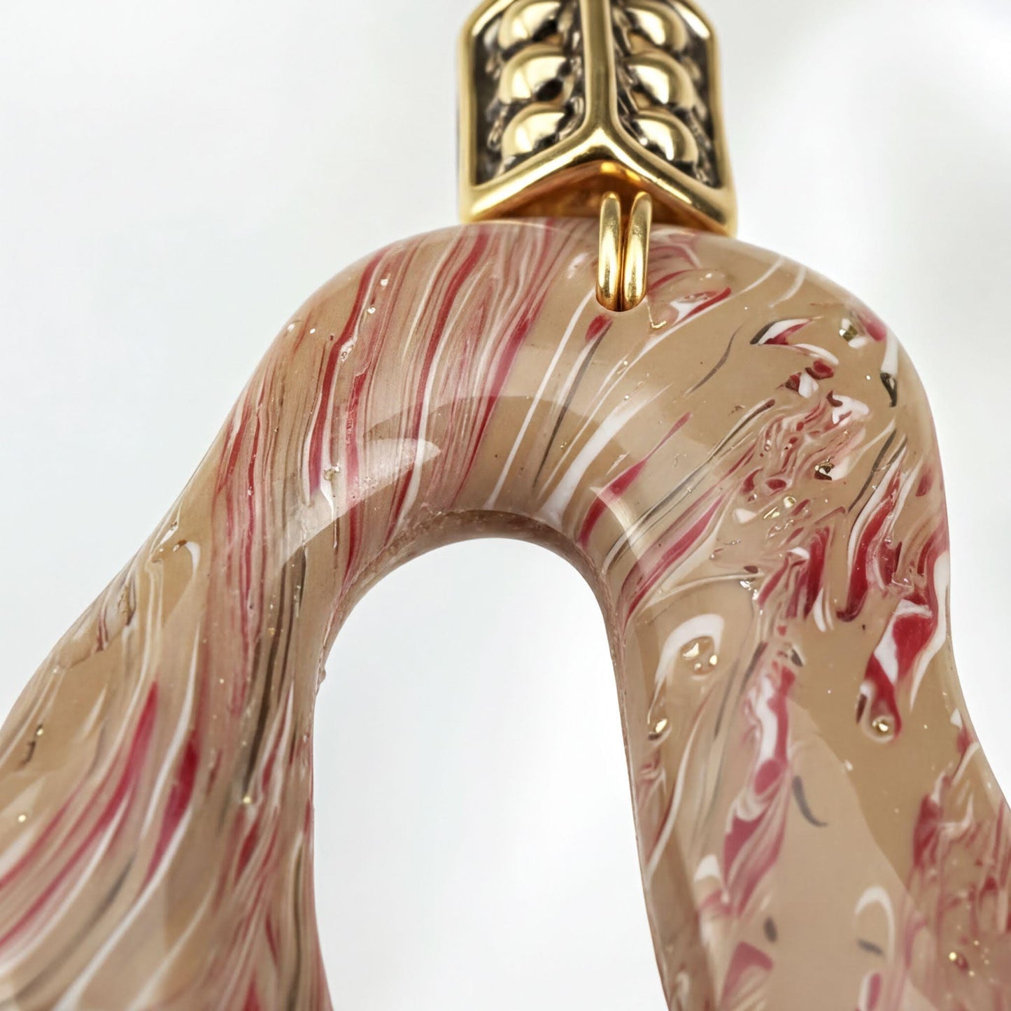 A close-up image of a decorative piece with a marbled pattern in shades of red and beige, featuring a gold-colored metal clasp.