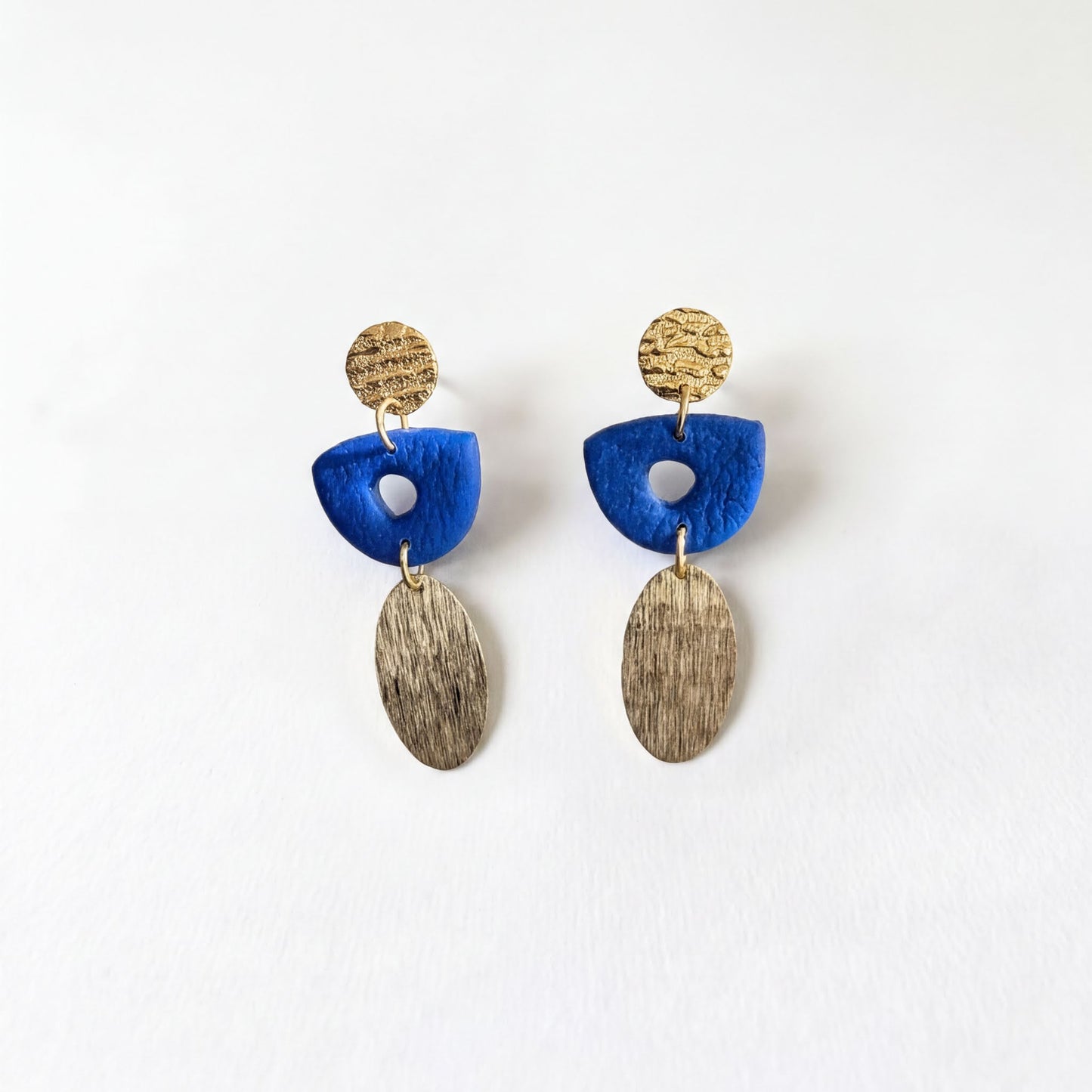 A pair of earrings with blue and gold elements, including a blue oval-shaped piece and a gold oval-shaped piece with a textured surface.