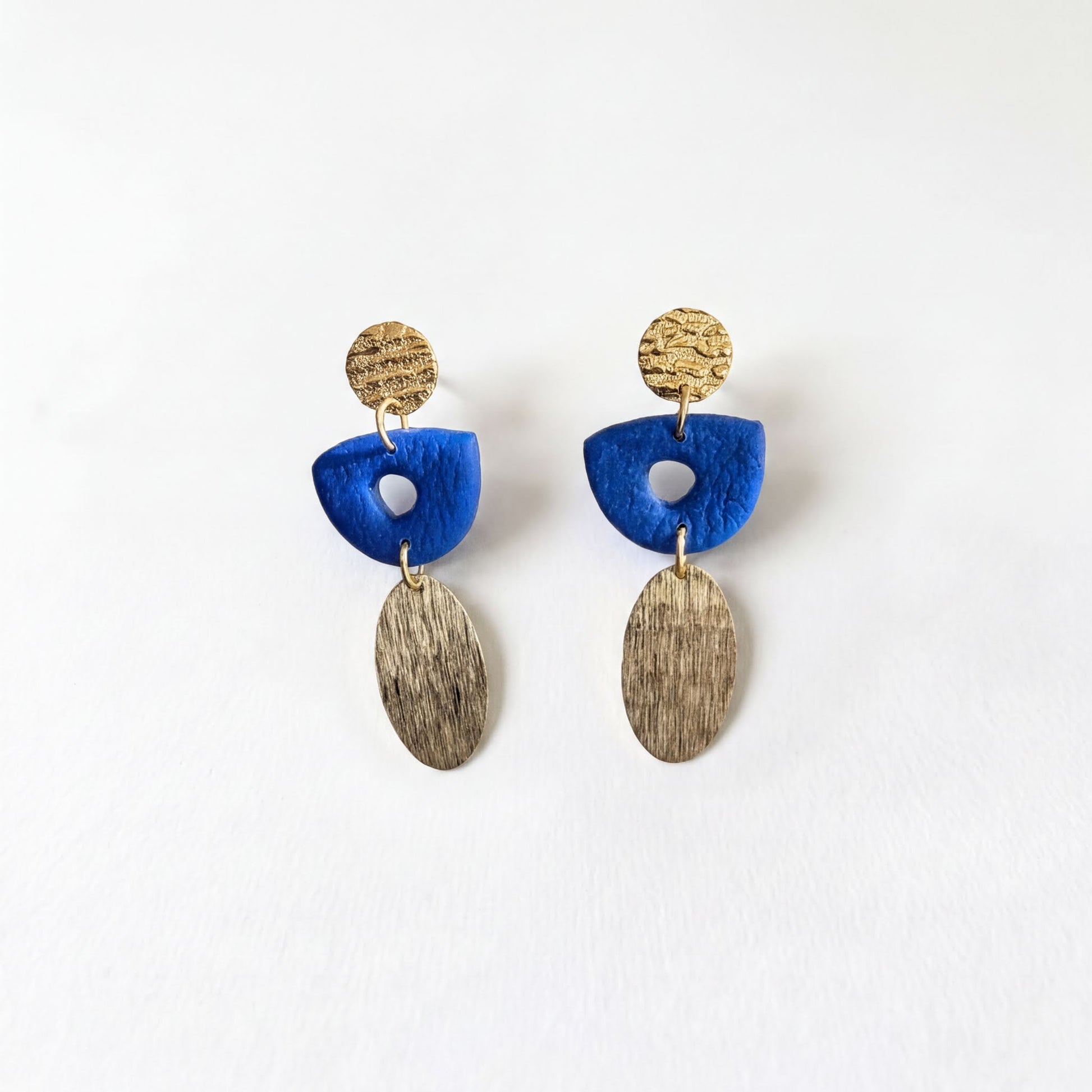 A pair of earrings with blue and gold elements, including a blue oval-shaped piece and a gold oval-shaped piece with a textured surface.